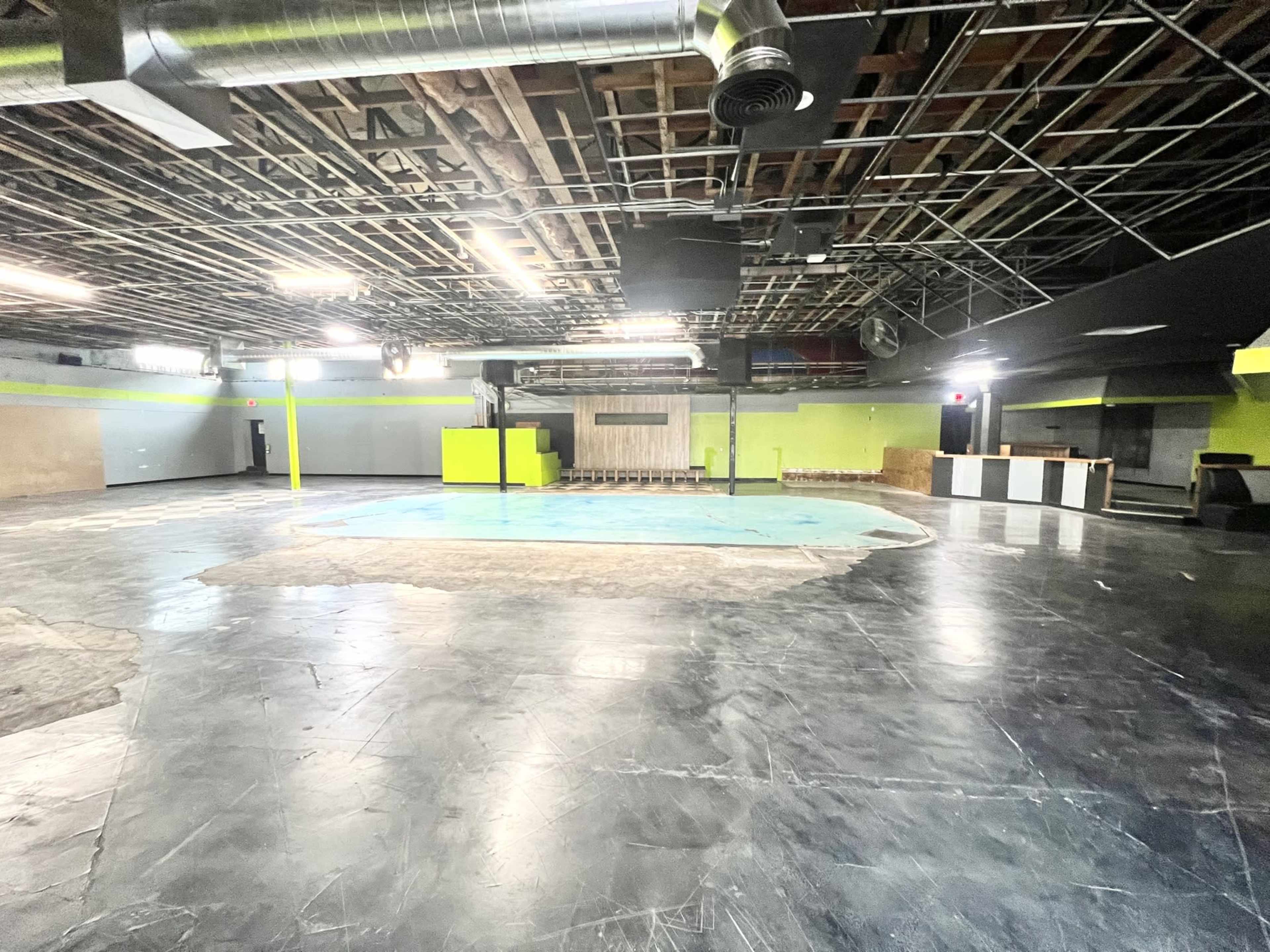 The image shows an empty event space with a partially filled pool area, exposed ceiling beams, and unfinished walls.