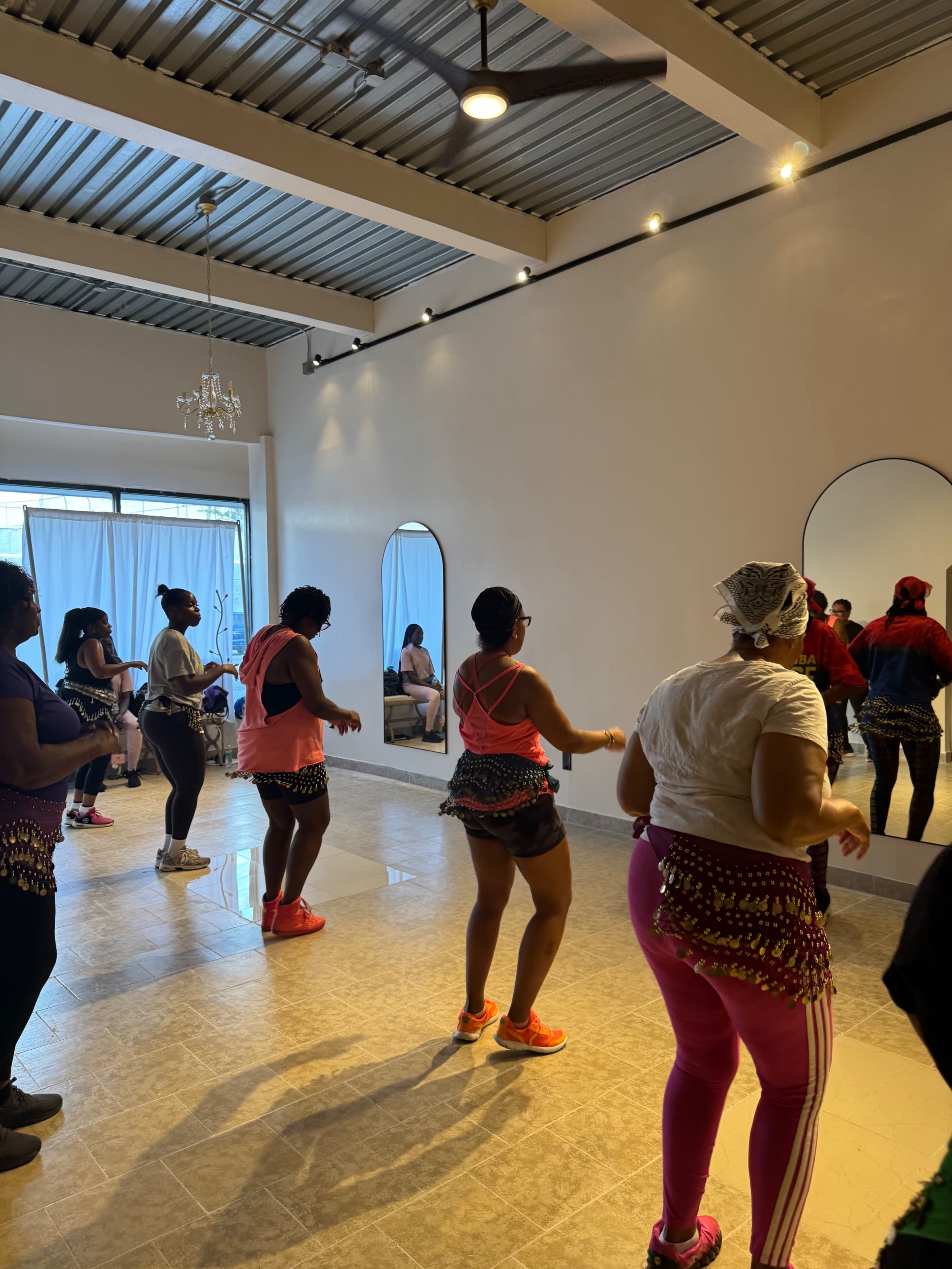 A group of individuals are participating in a dance class in a spacious studio with mirrors and large windows.