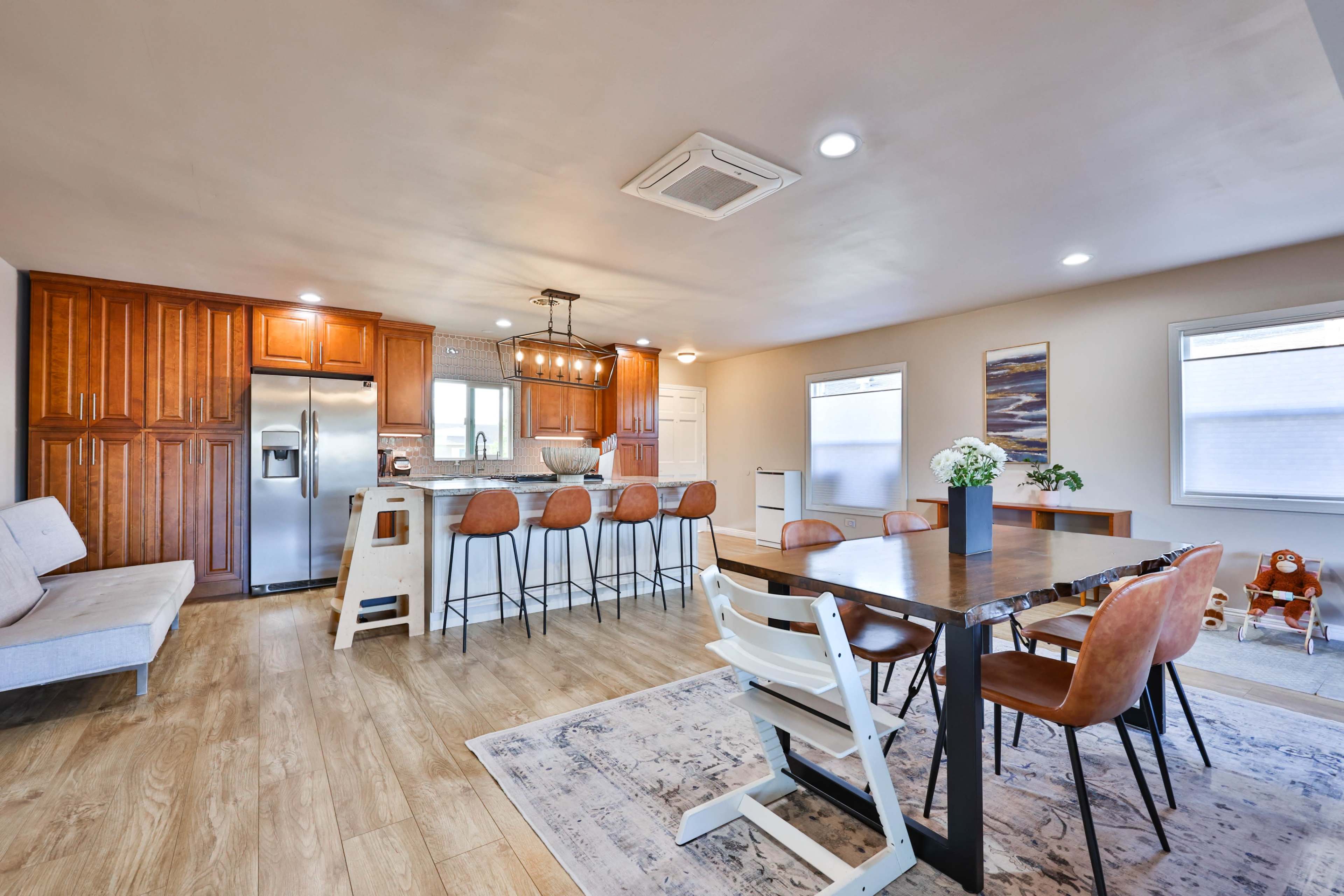 A modern kitchen and dining area featuring wooden cabinets, a large island with bar seating, and a dining table with six chairs.