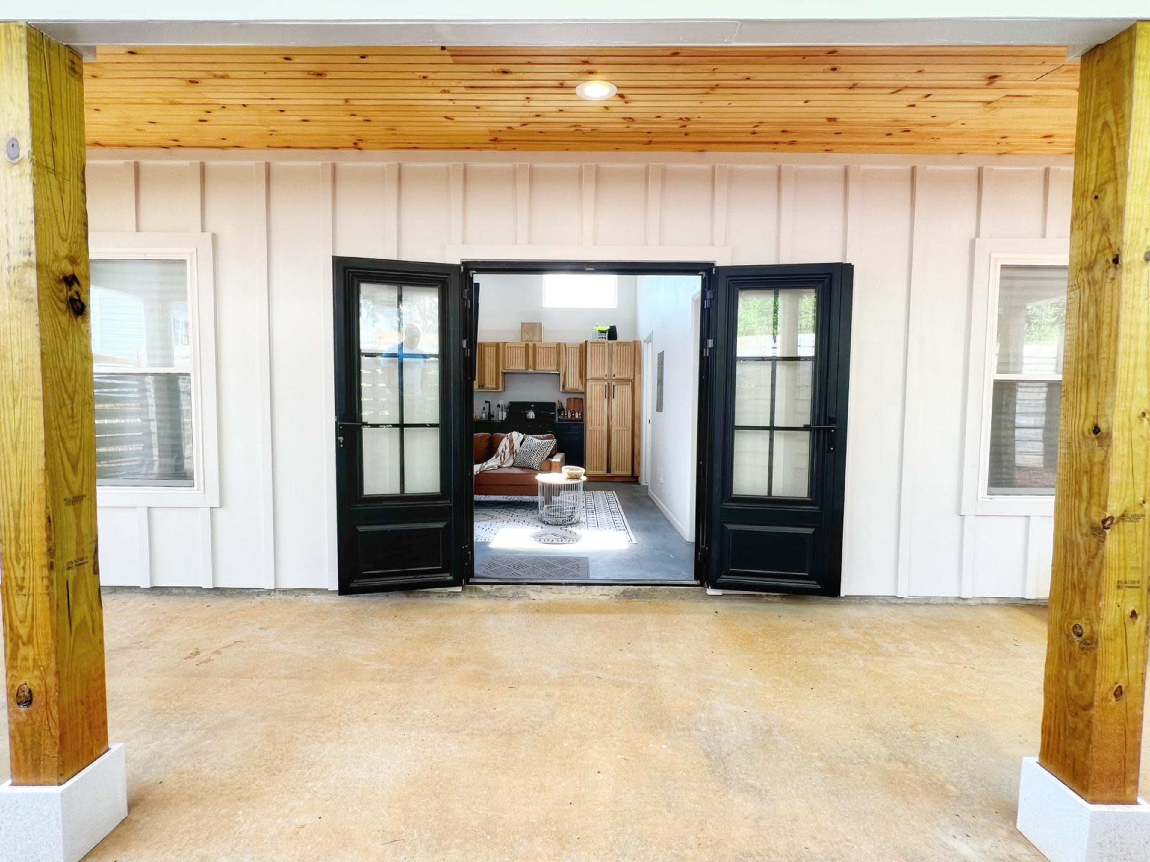 An open entrance with double black doors leading into a light-colored interior space featuring a kitchen and living area.