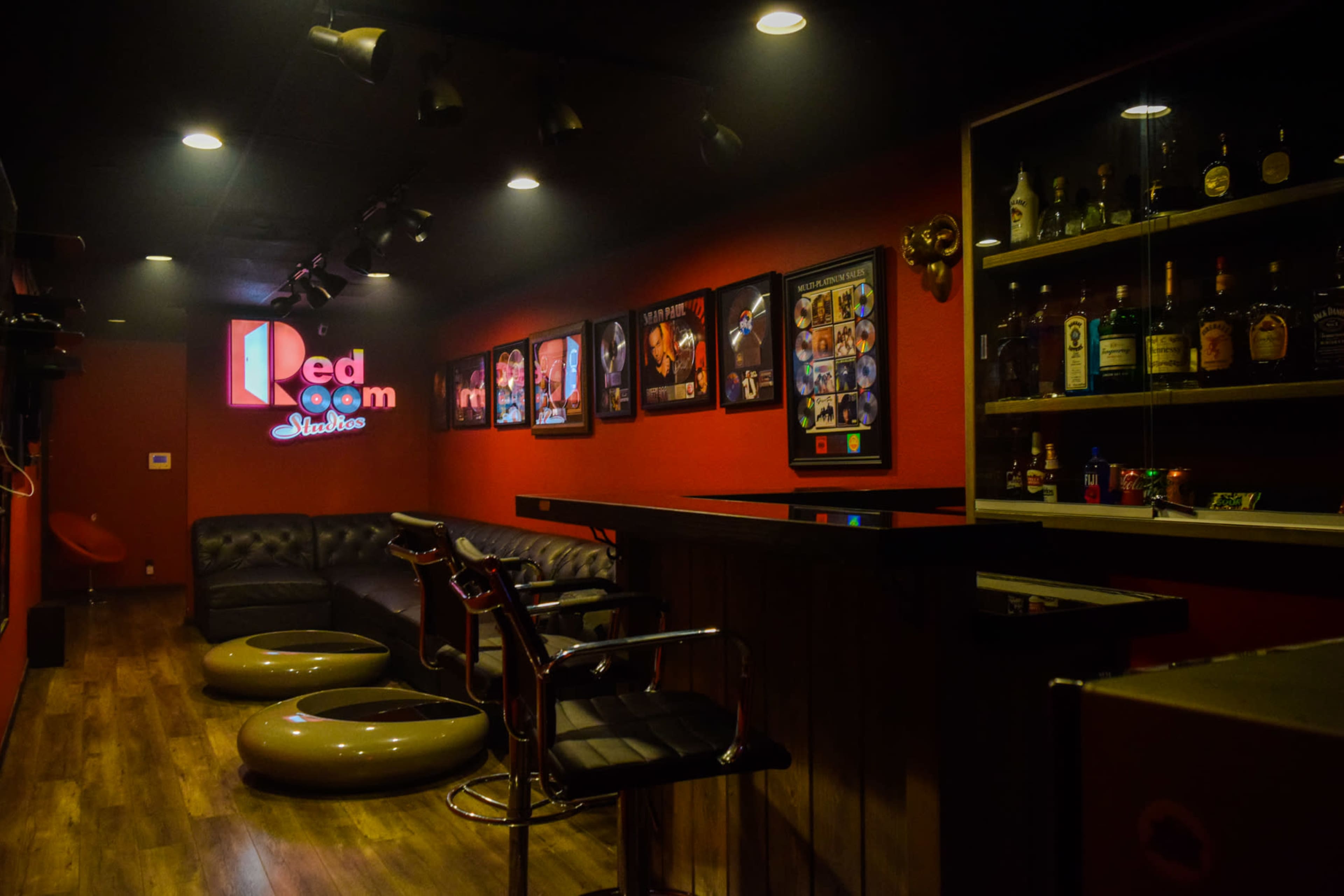 The image shows a dimly lit lounge with red walls, a bar setup, and several framed pictures on the walls.