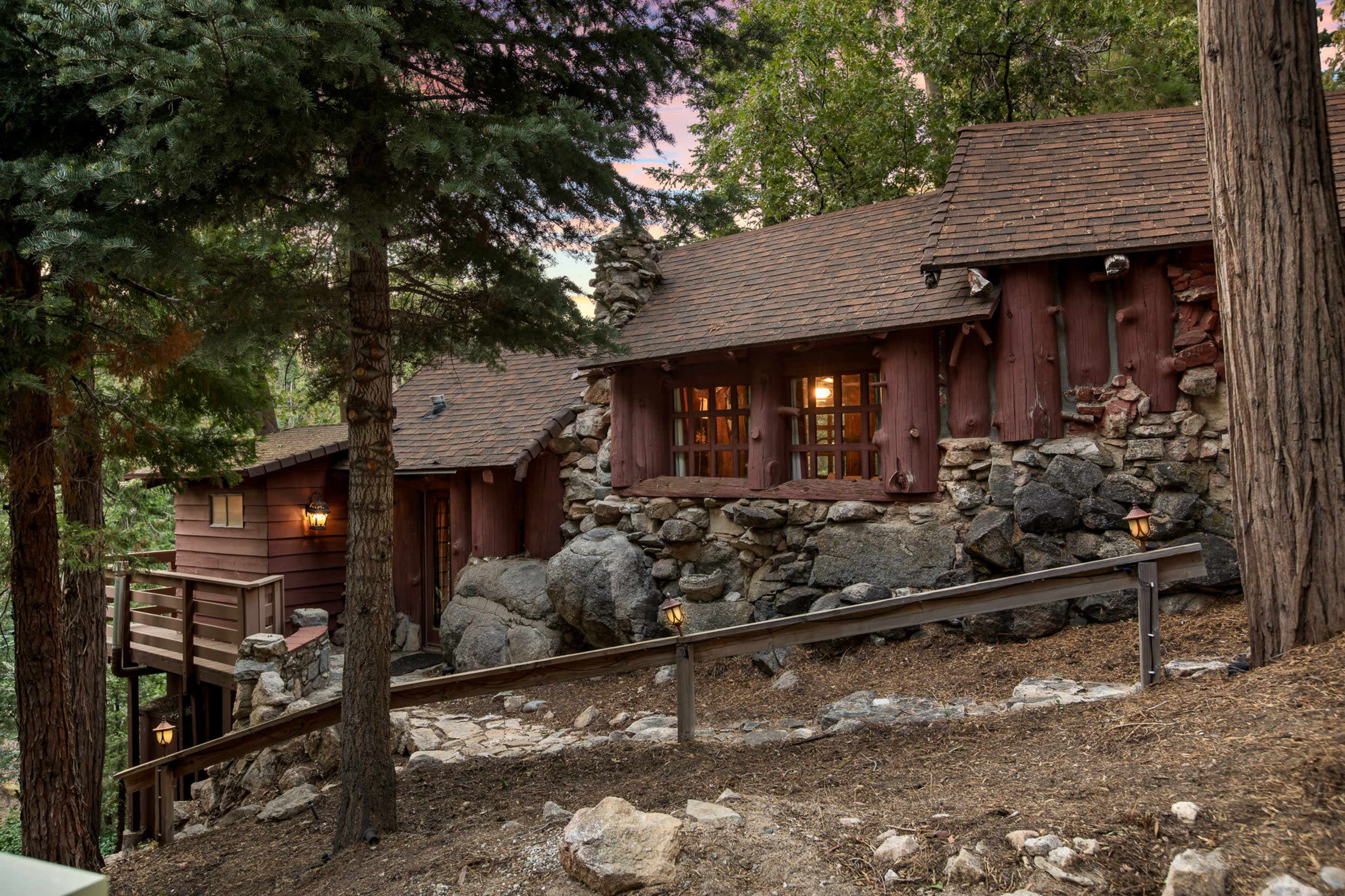 A rustic cabin made of wood and stone sits nestled among tall trees on a sloped landscape.
