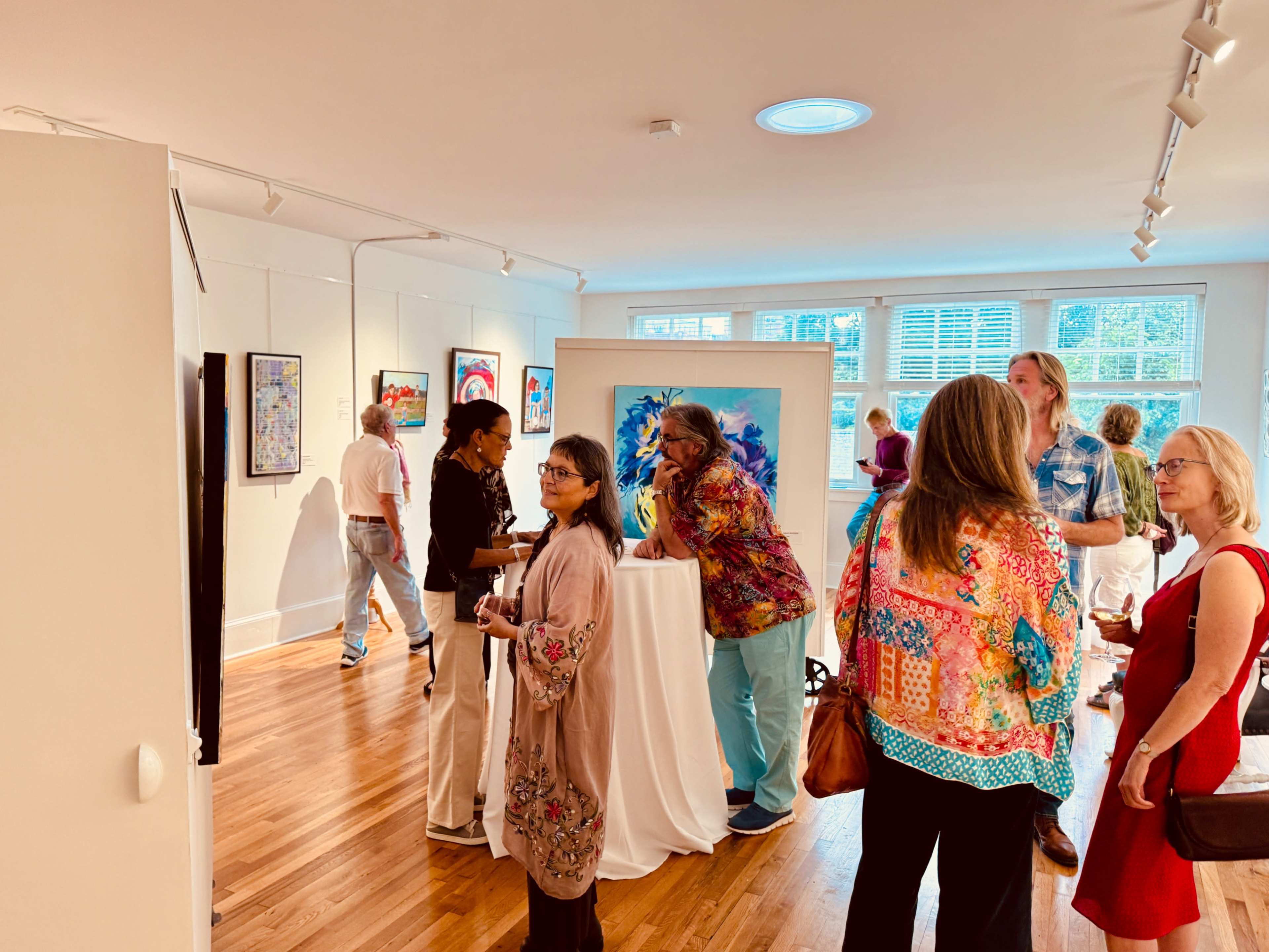 A group of people socialize at an art gallery amidst various artworks displayed on the walls.