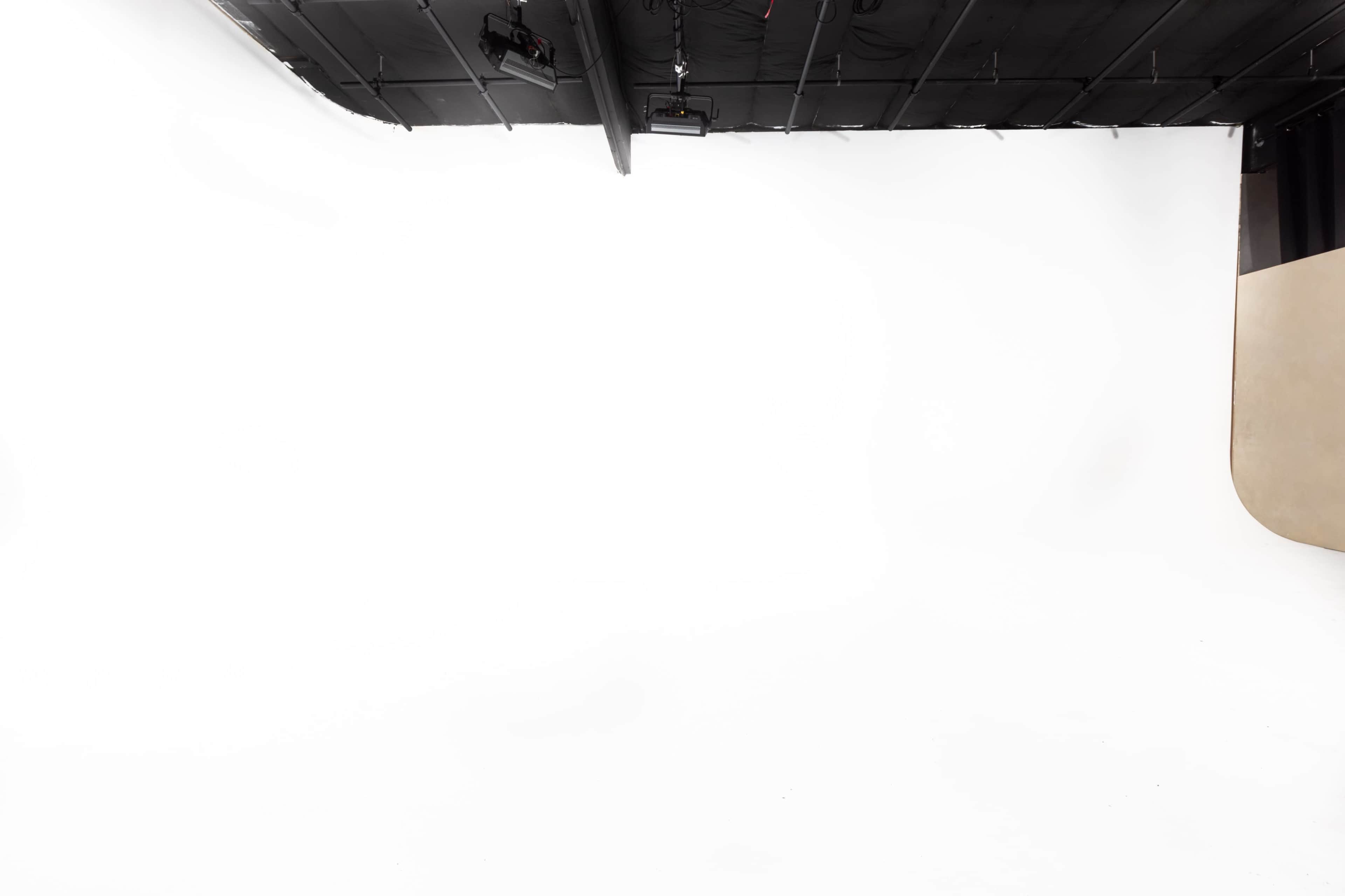 The image shows a spacious photography studio with a white backdrop and a curved beige section on one side.