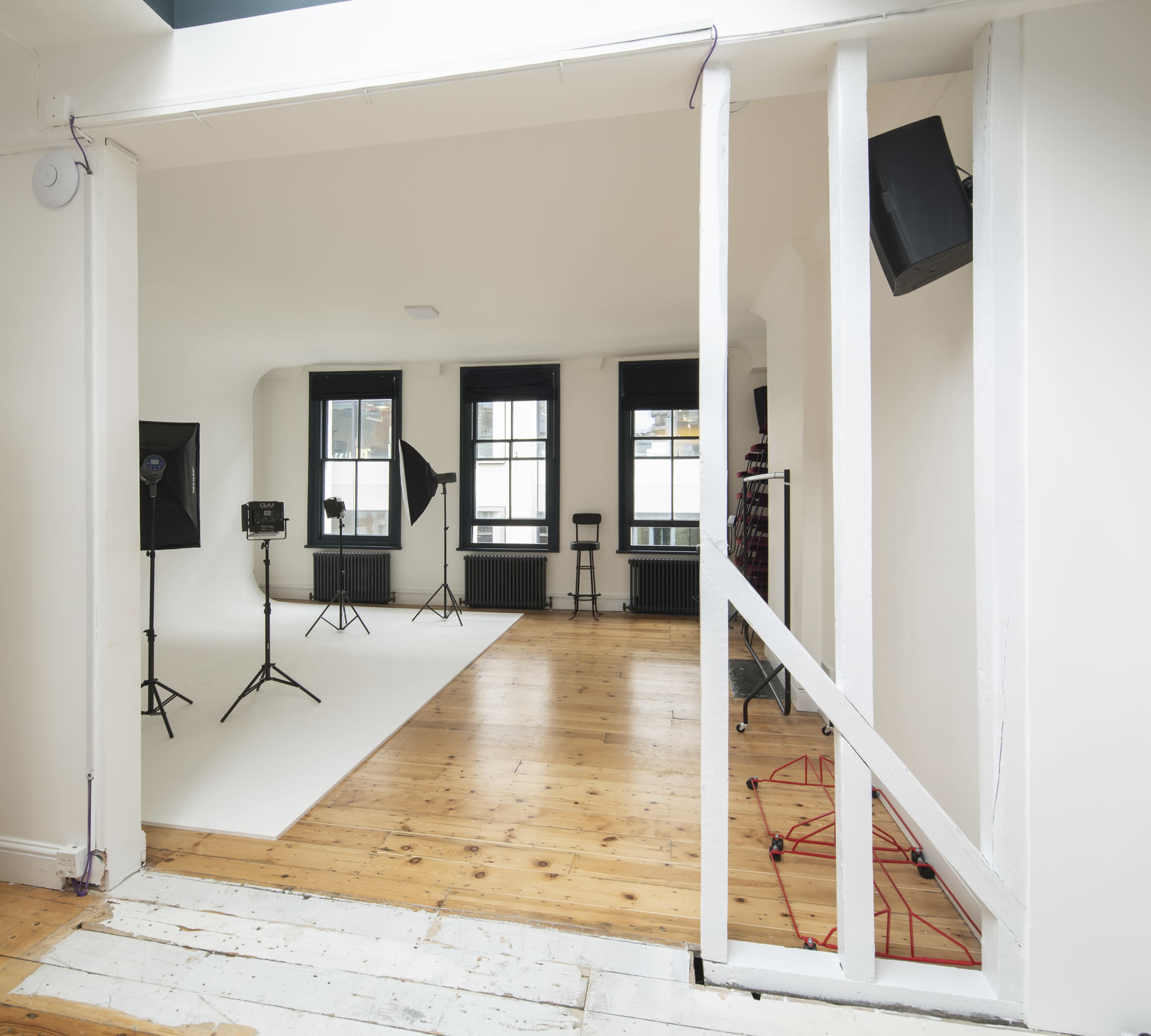 A photography studio with a clean, white backdrop, lighting equipment, and wooden flooring.