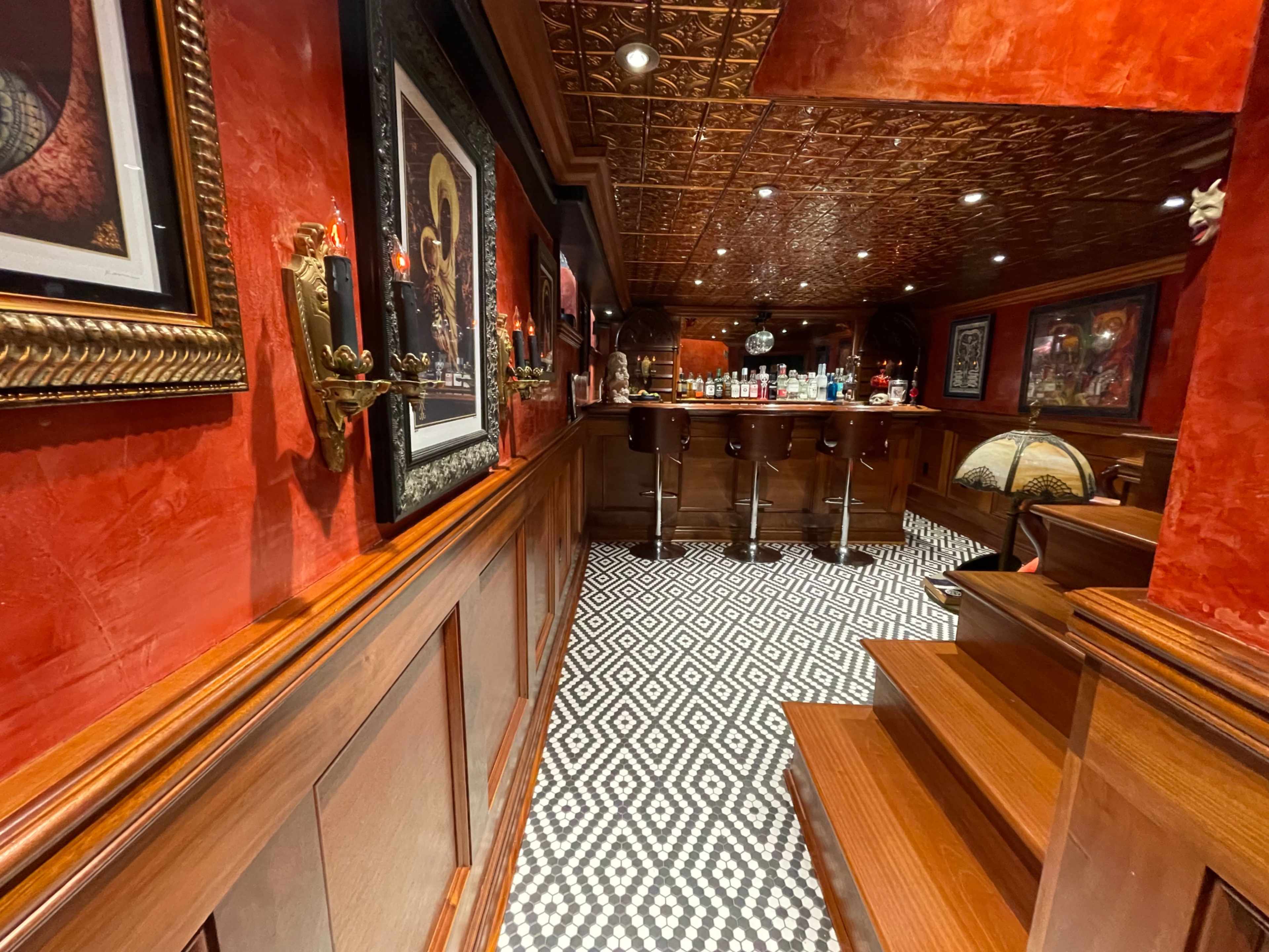 The image shows an upscale bar area with dark wood paneling, patterned tile flooring, and a well-stocked backlit bar.