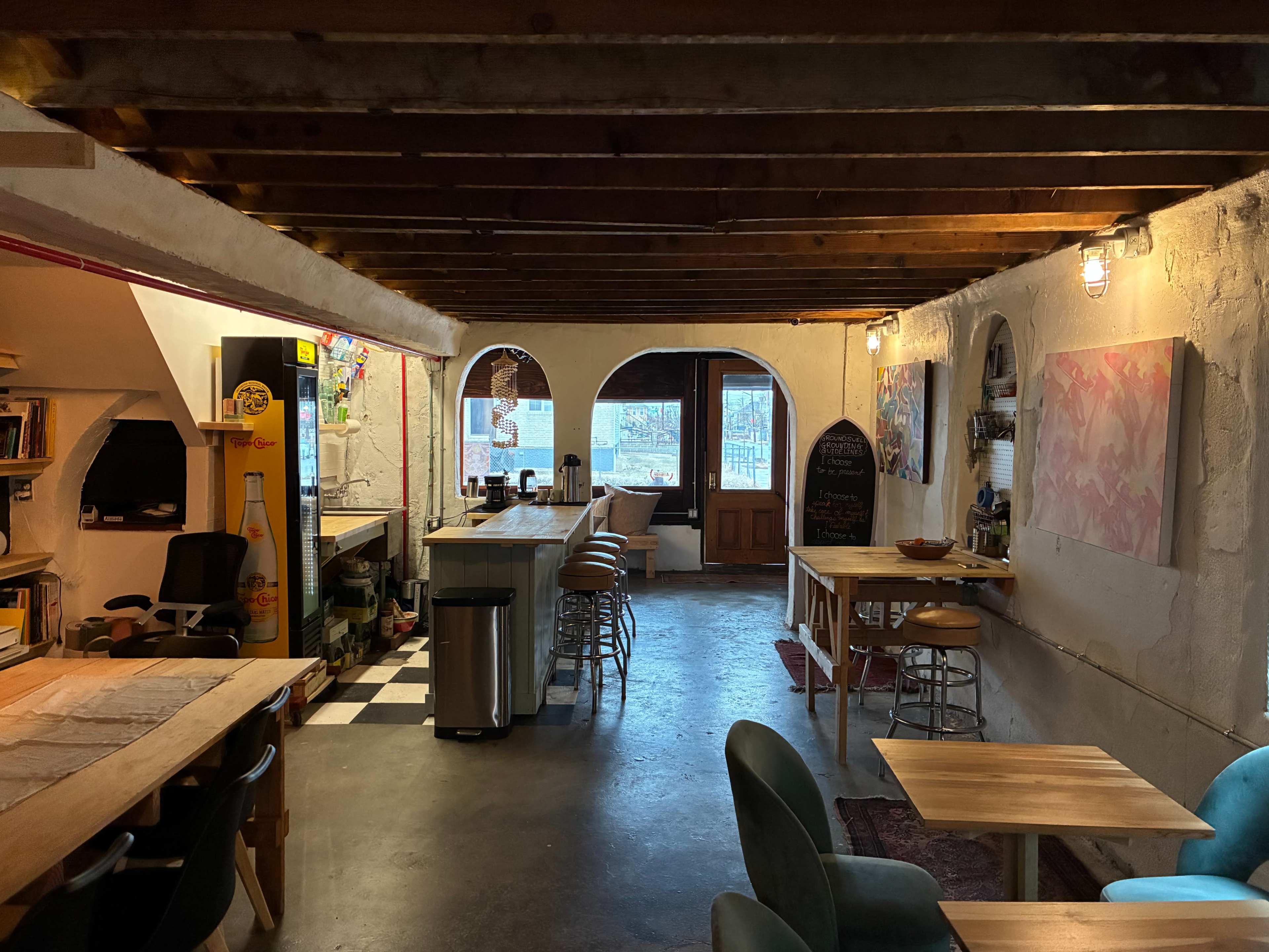 The image shows a cozy café interior with wooden beams, tables, and an open layout featuring a service area and archway windows.