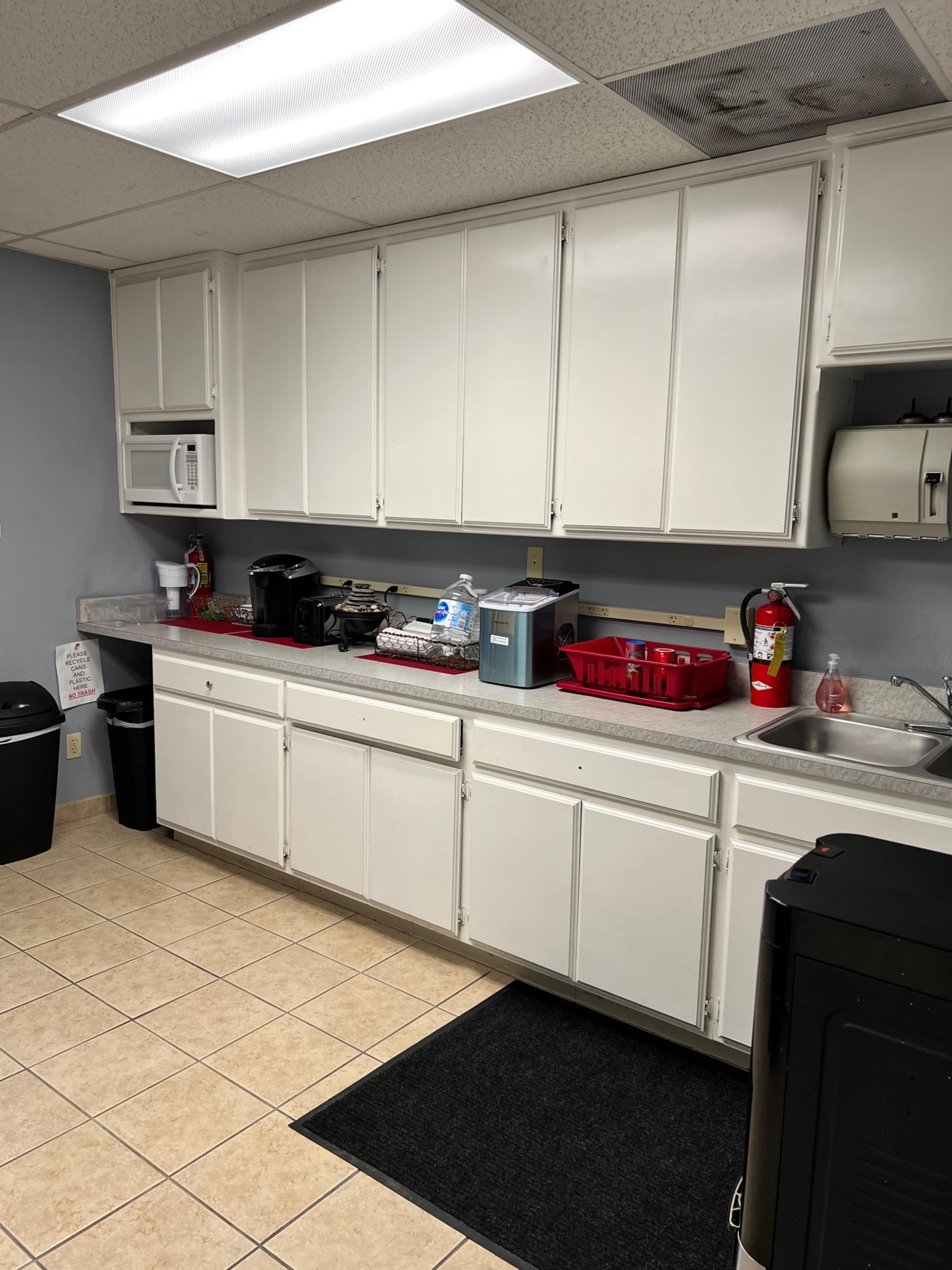 A kitchen area featuring white cabinets, a countertop with various appliances and utensils, and tiled flooring.