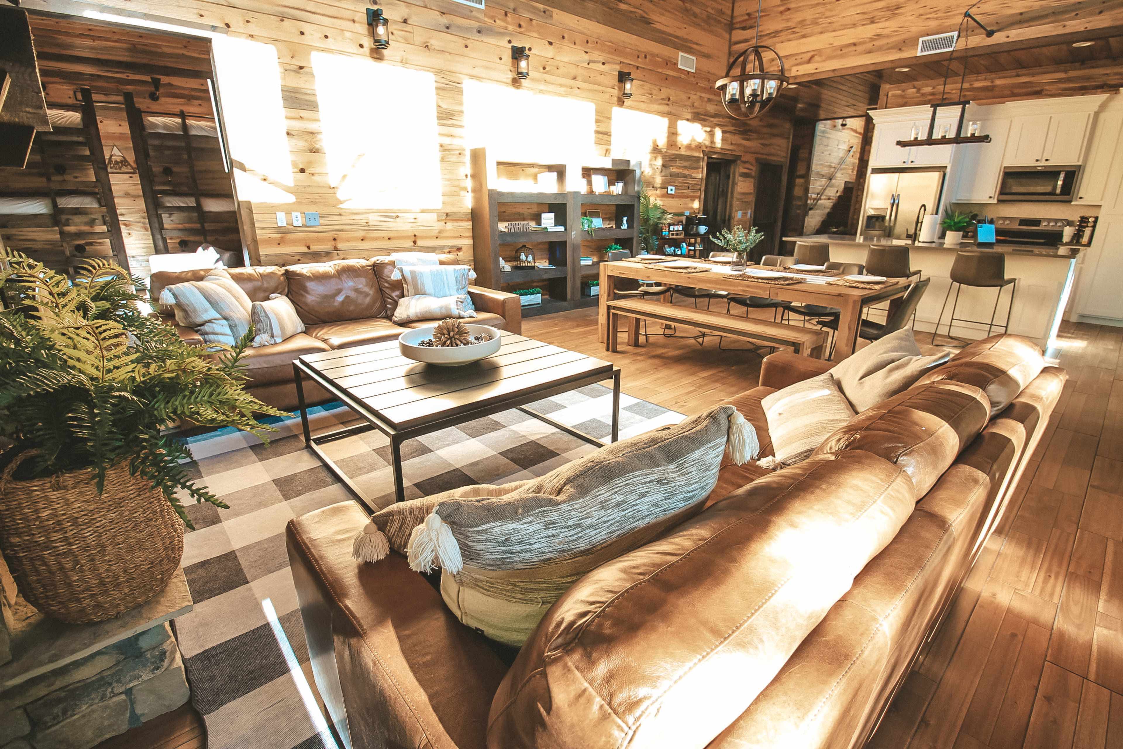 A warm, rustic living room with leather sofas, a wooden dining table, and large windows that let in natural light.