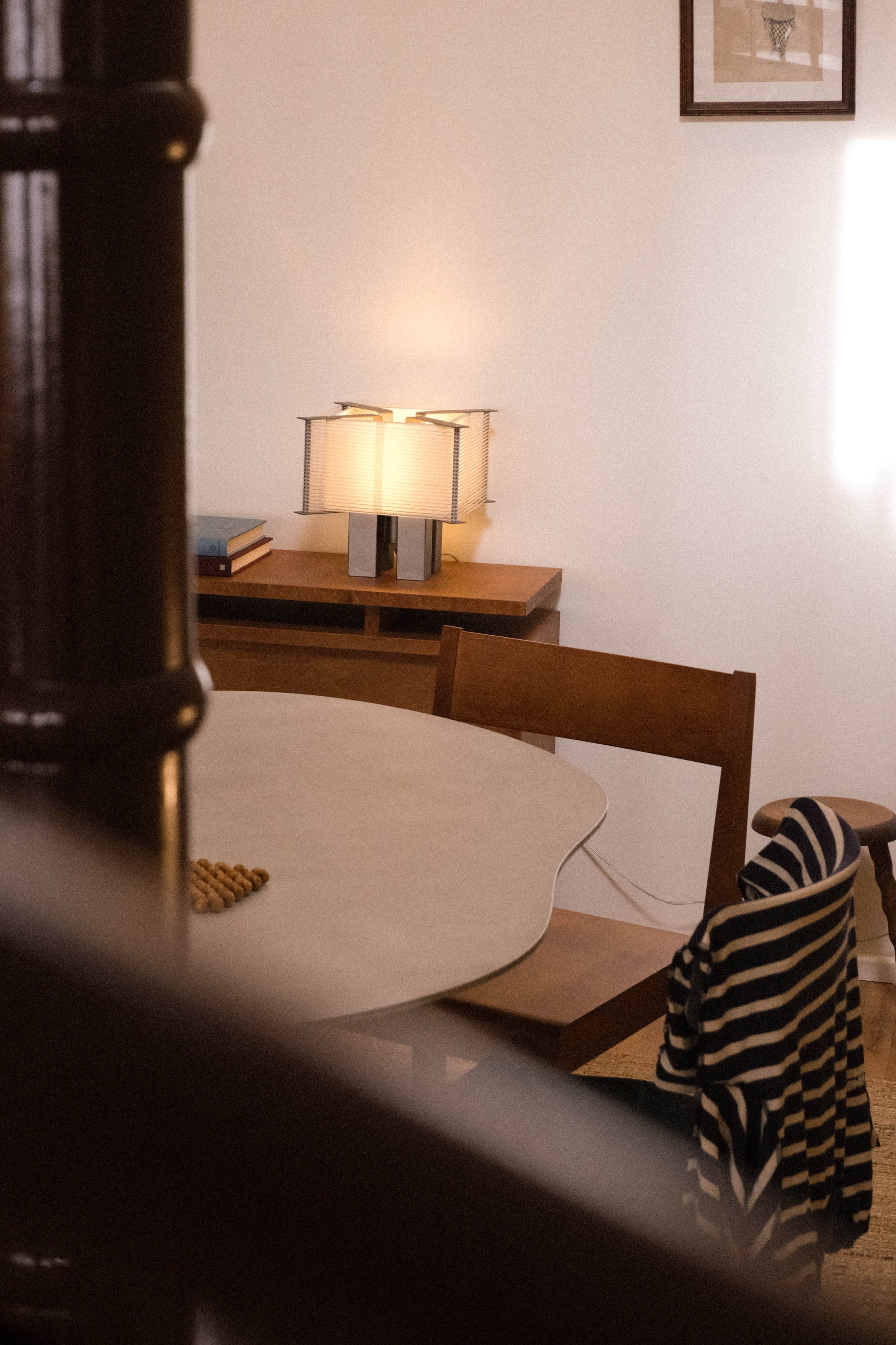 A wooden table and chairs are set in a softly lit room, with a lamp providing illumination on a side surface.