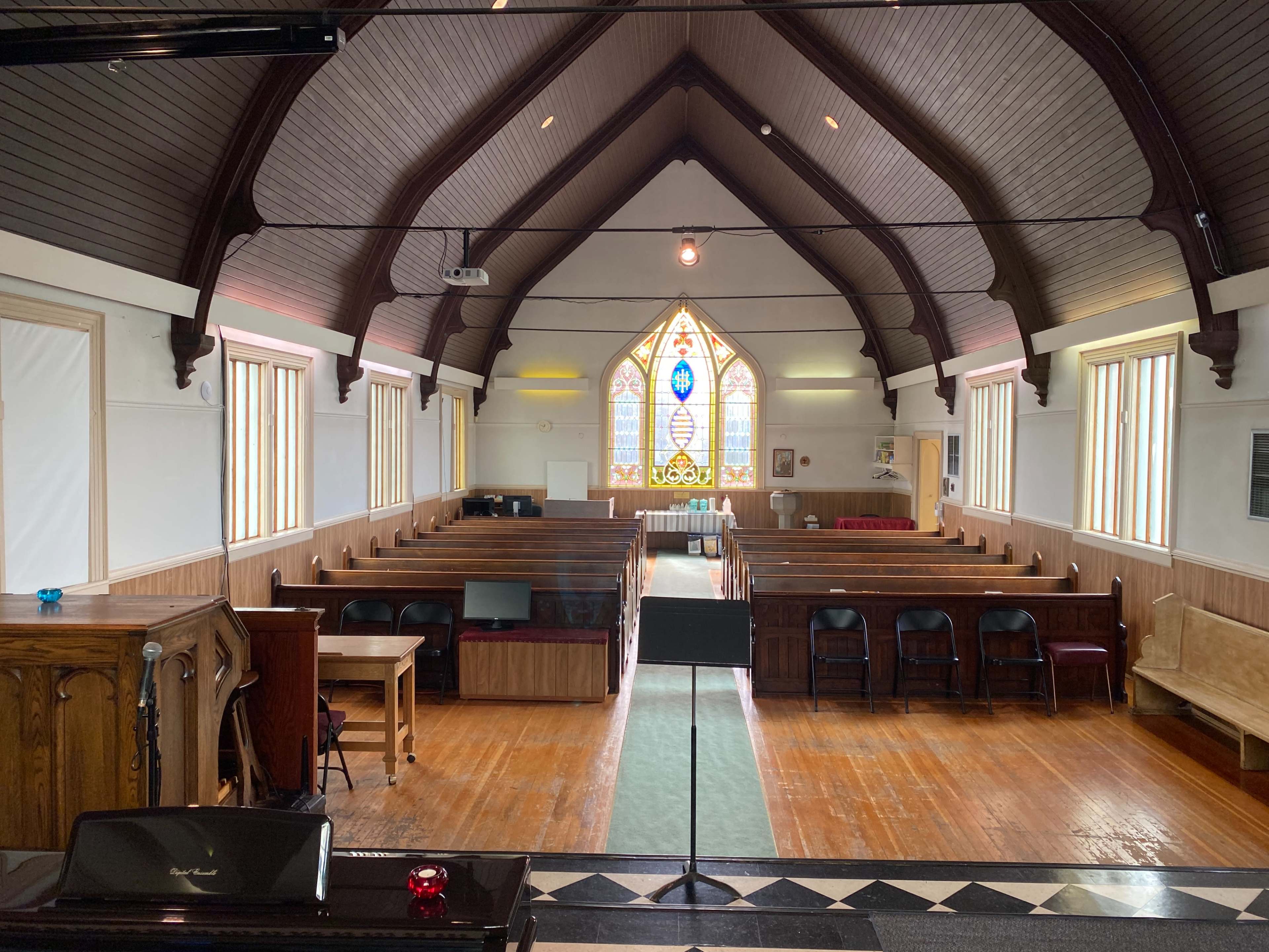 The interior of a church features wooden pews arranged facing the front, with a stained glass window illuminating the space.