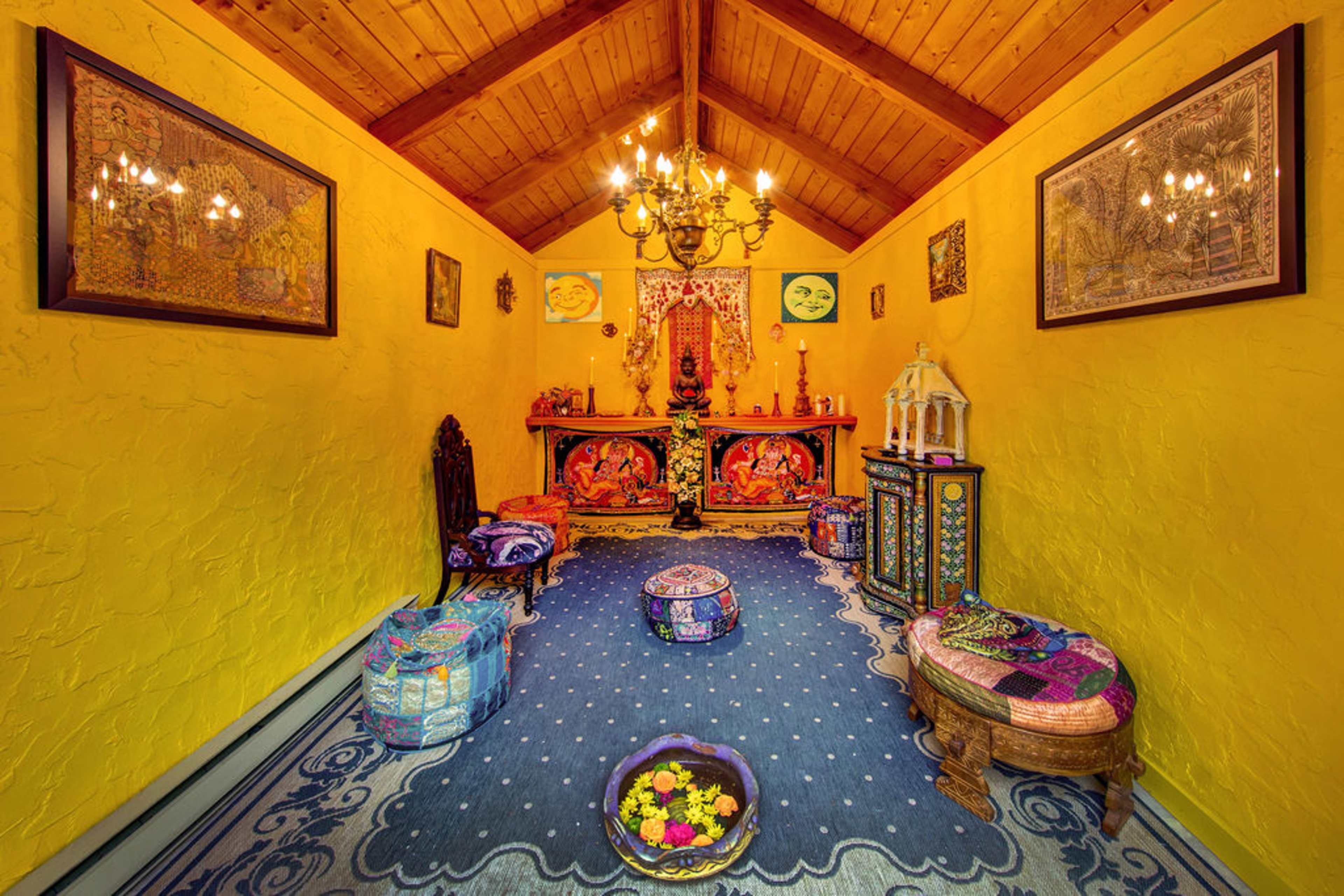 A brightly colored room with a wooden ceiling, featuring decorative artwork, a central altar with religious statues, and various seating arrangements.
