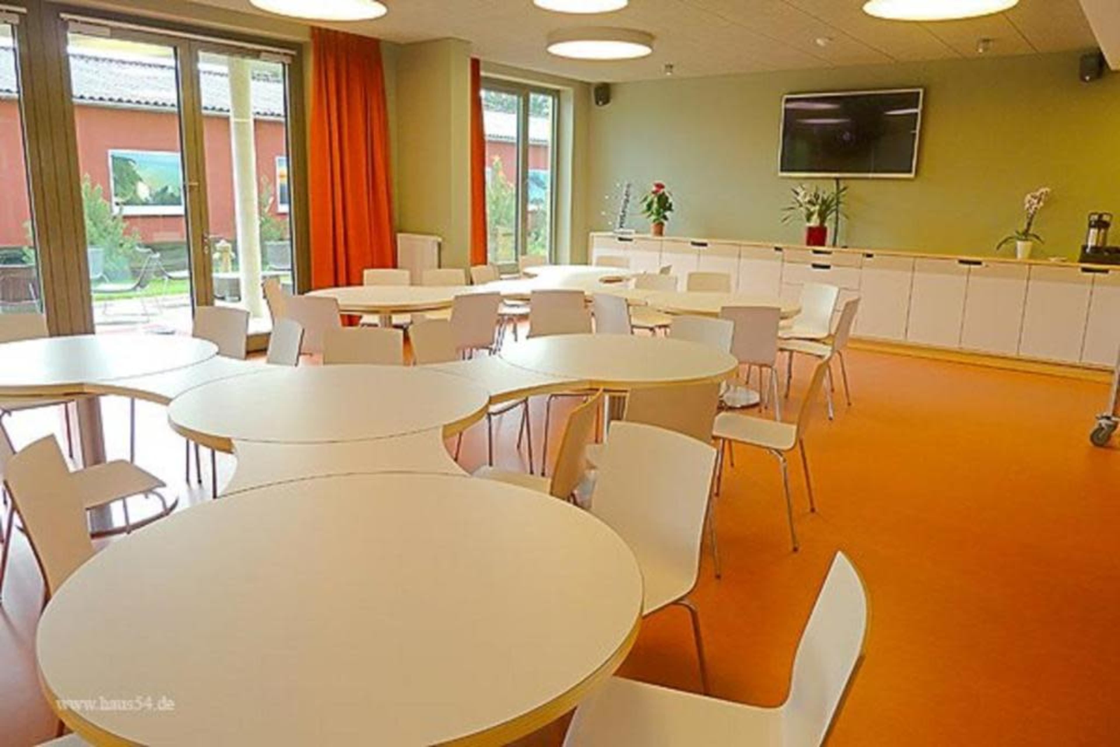 A modern meeting room with several round tables and white chairs, featuring large windows that provide natural light.