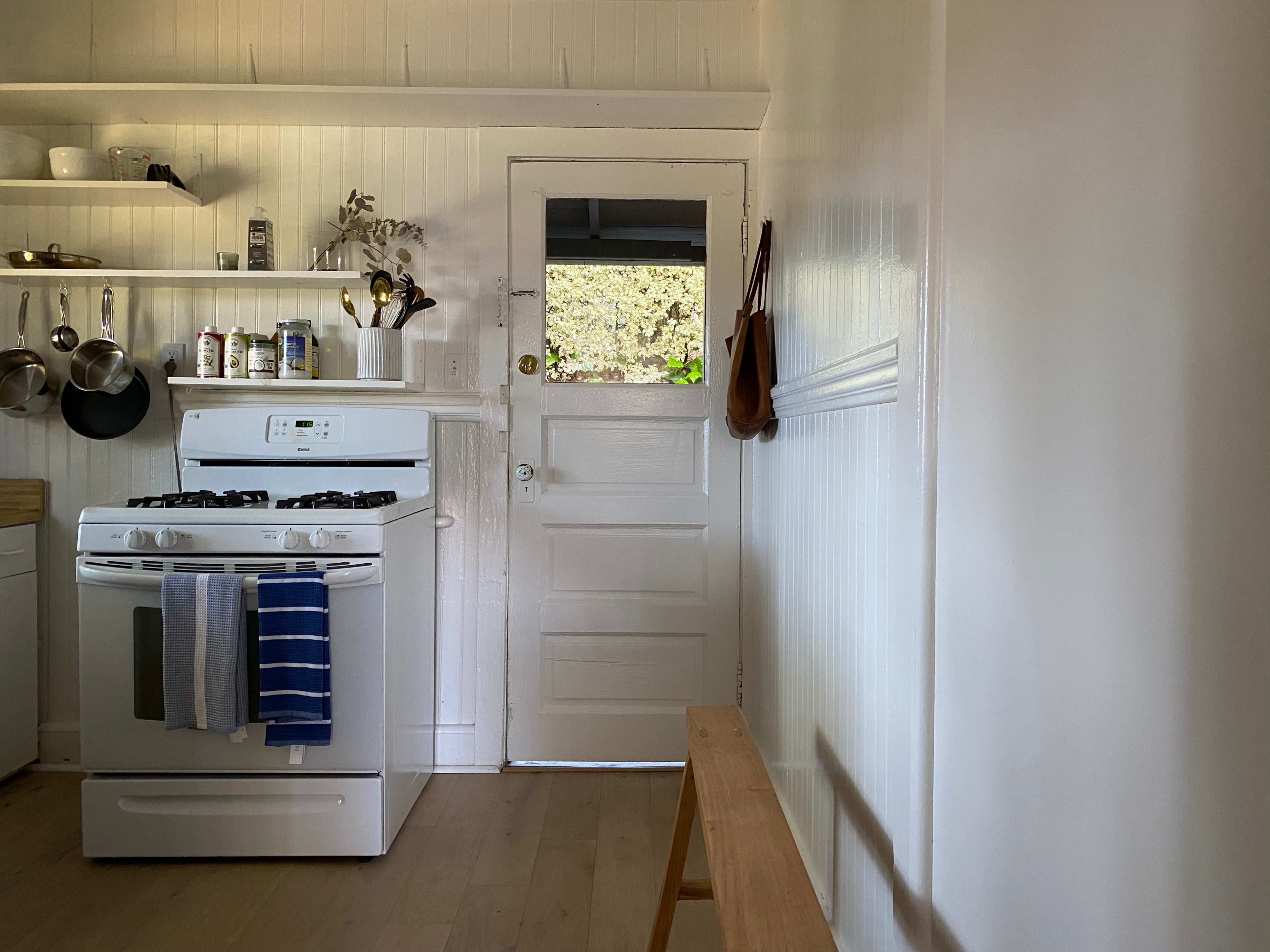 A clean kitchen features a white stove, shelves with kitchenware, and a door leading outside.