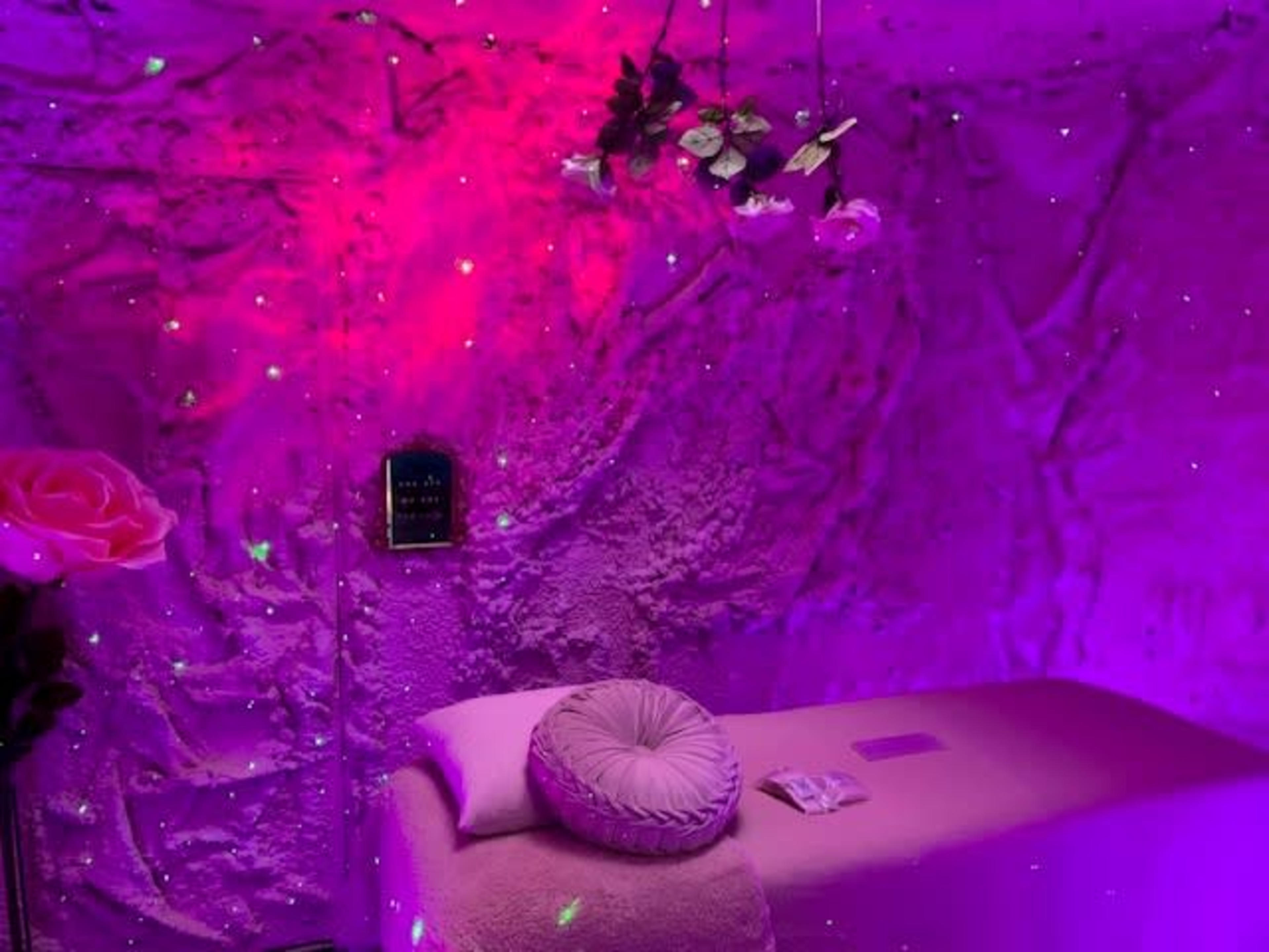 A treatment room with a massage table surrounded by purple walls and decorative floral elements.