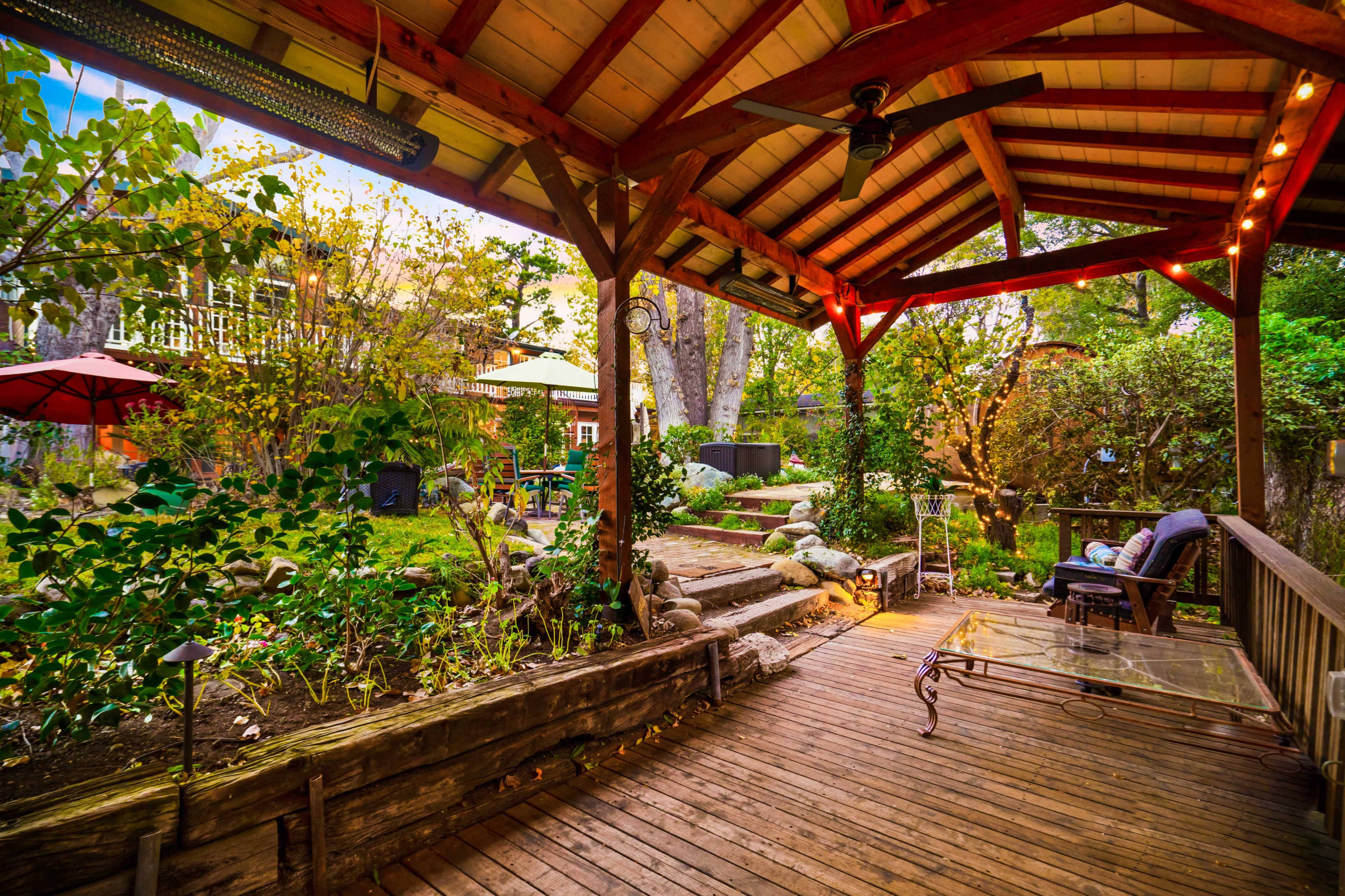 A wooden deck with a covered pergola overlooks a garden filled with plants and seating areas.