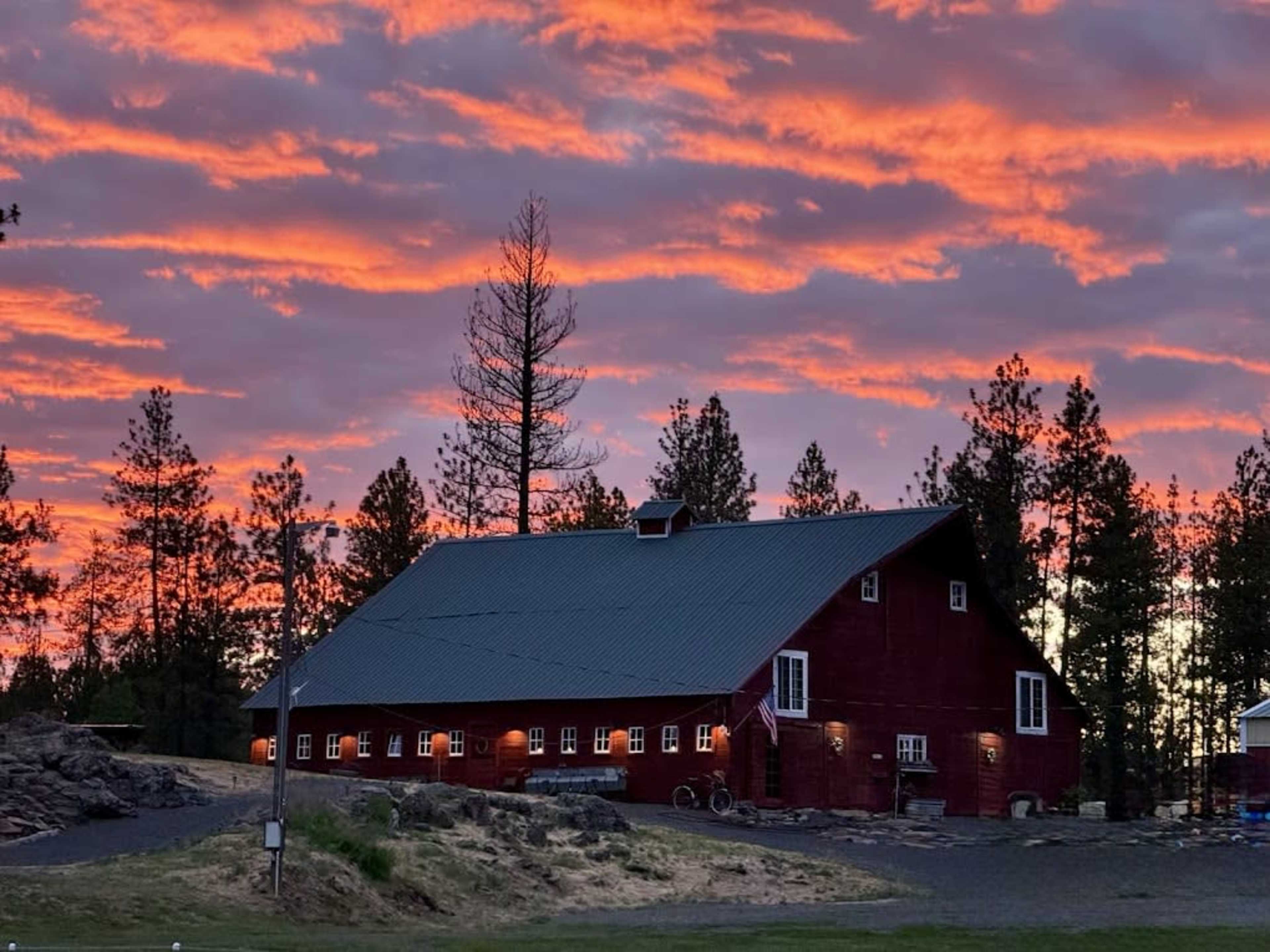 A red barn stands in silhouette against a vibrant sunset sky filled with clouds.