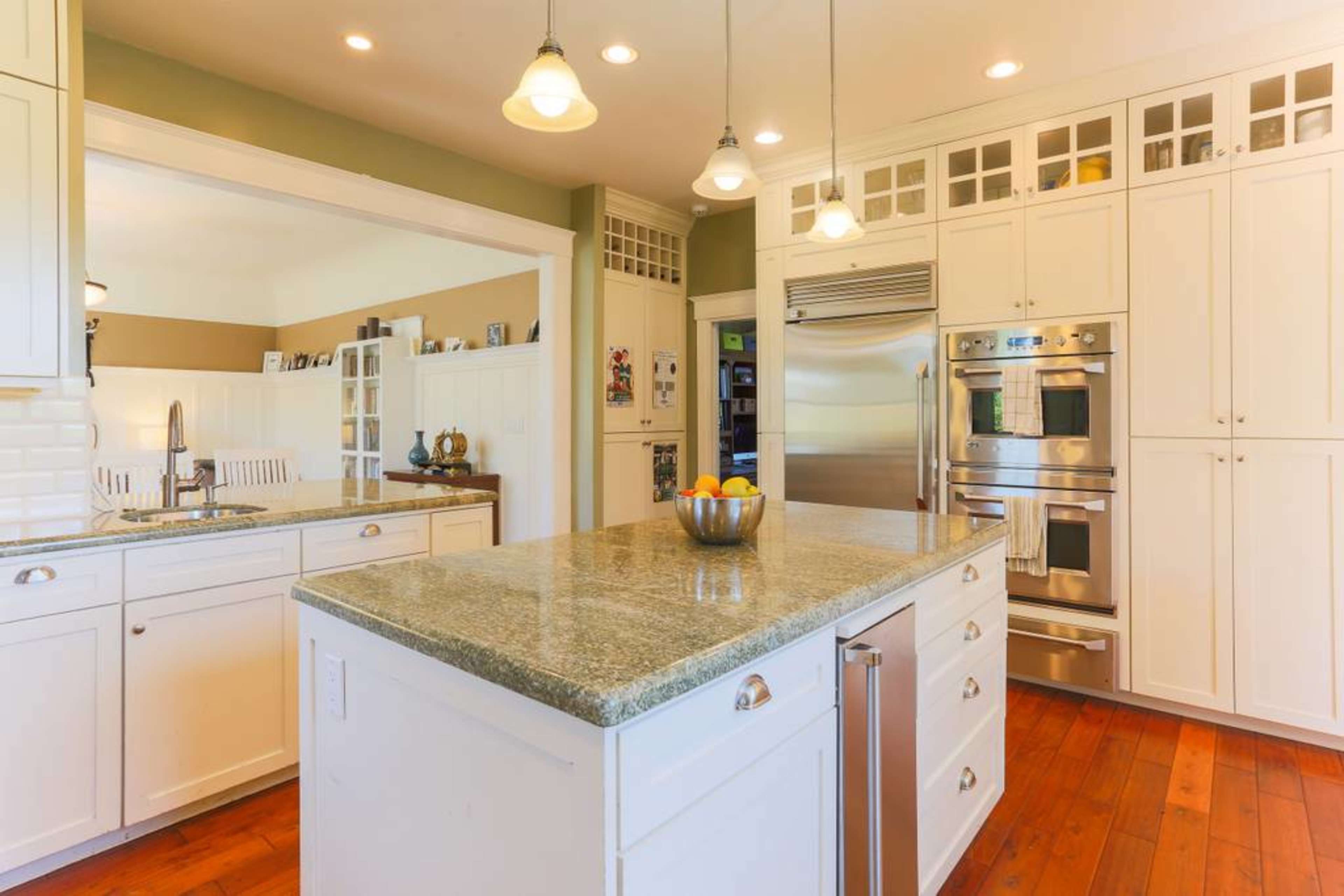 A spacious kitchen with white cabinets, a large granite island, and modern stainless steel appliances.