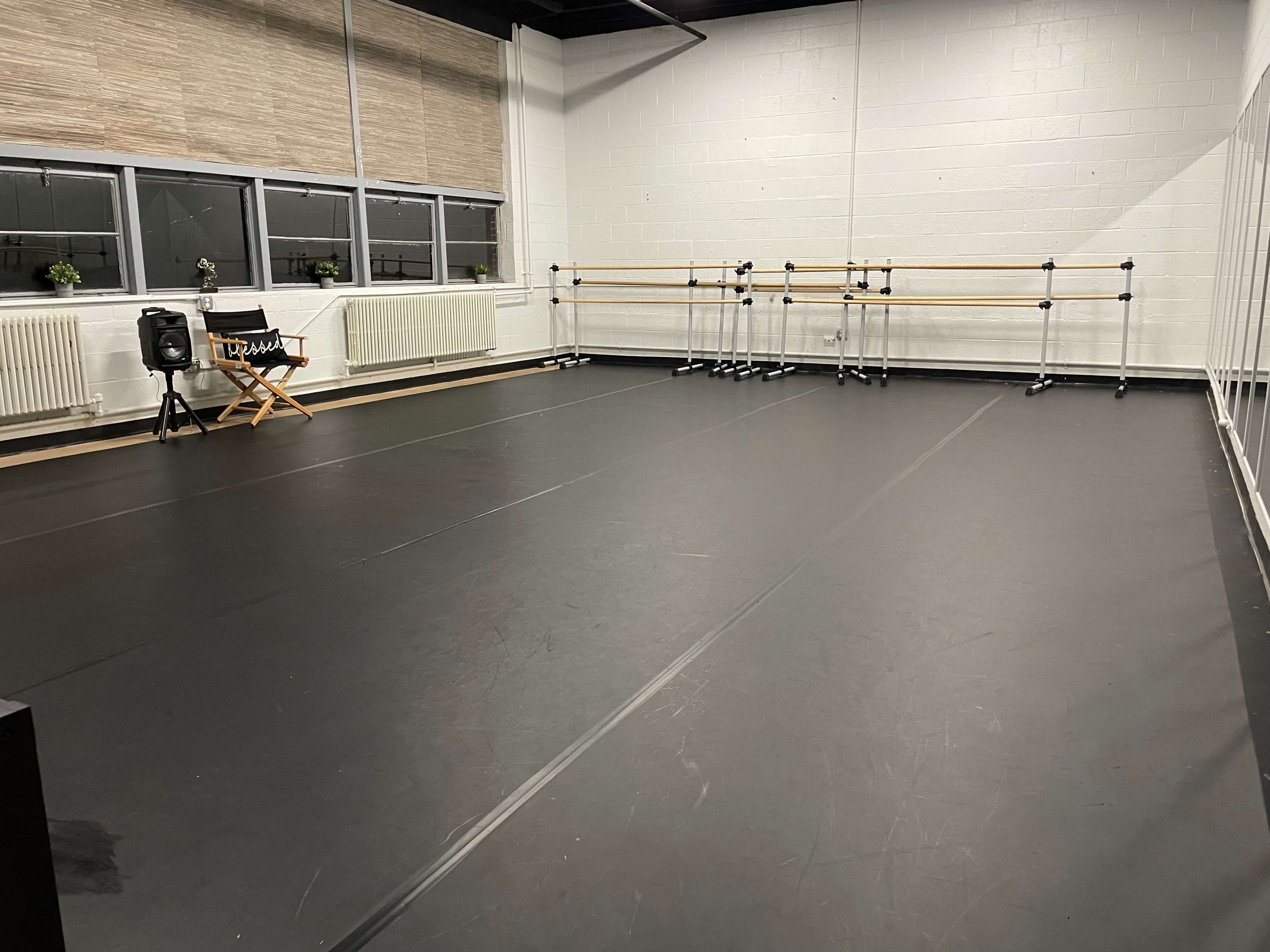 A spacious dance studio with a black floor, wall mirrors, and wooden ballet barres along one side.