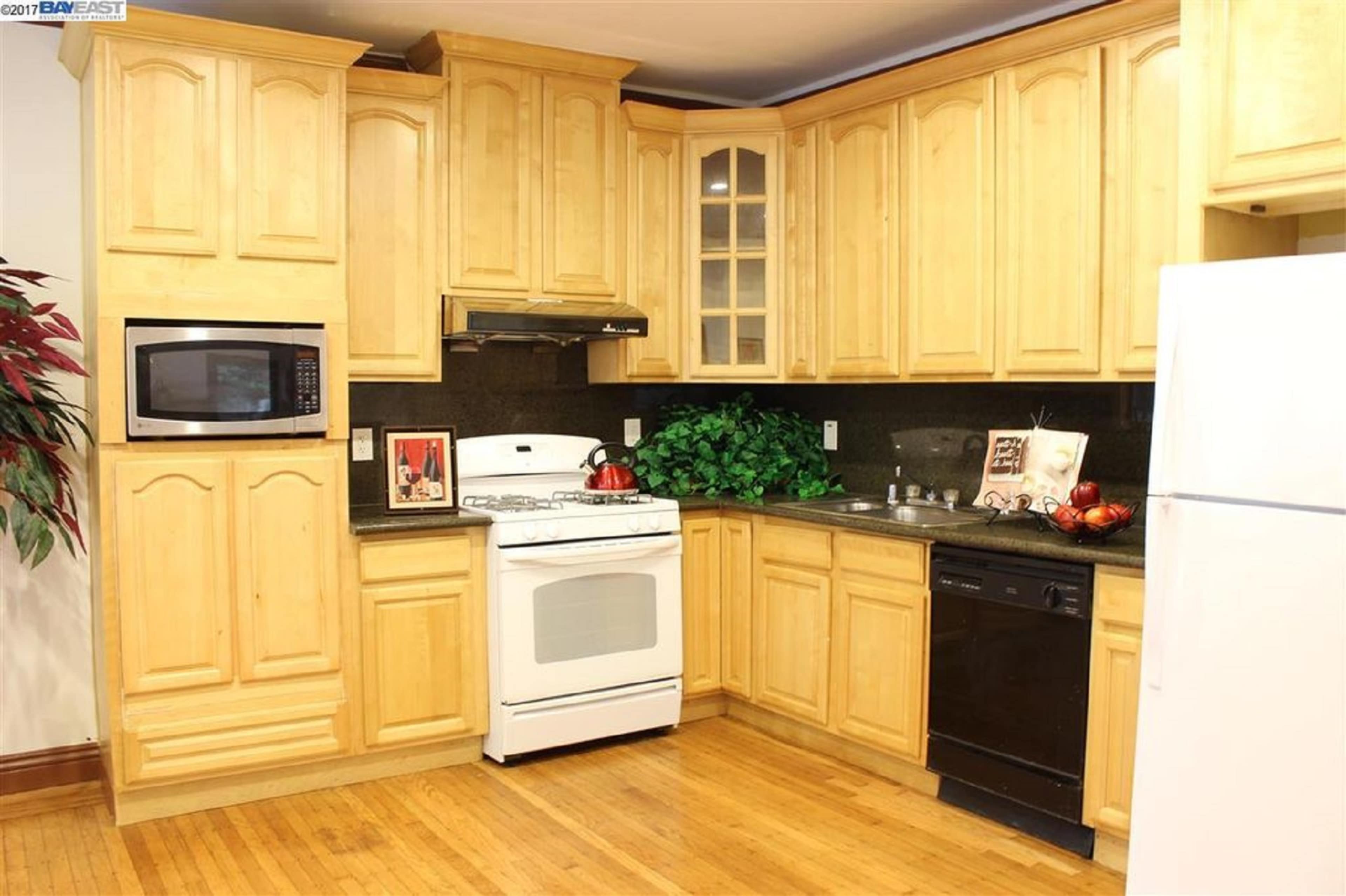 A kitchen with wooden cabinets, a white stove, a microwave, a dishwasher, and dark countertops.