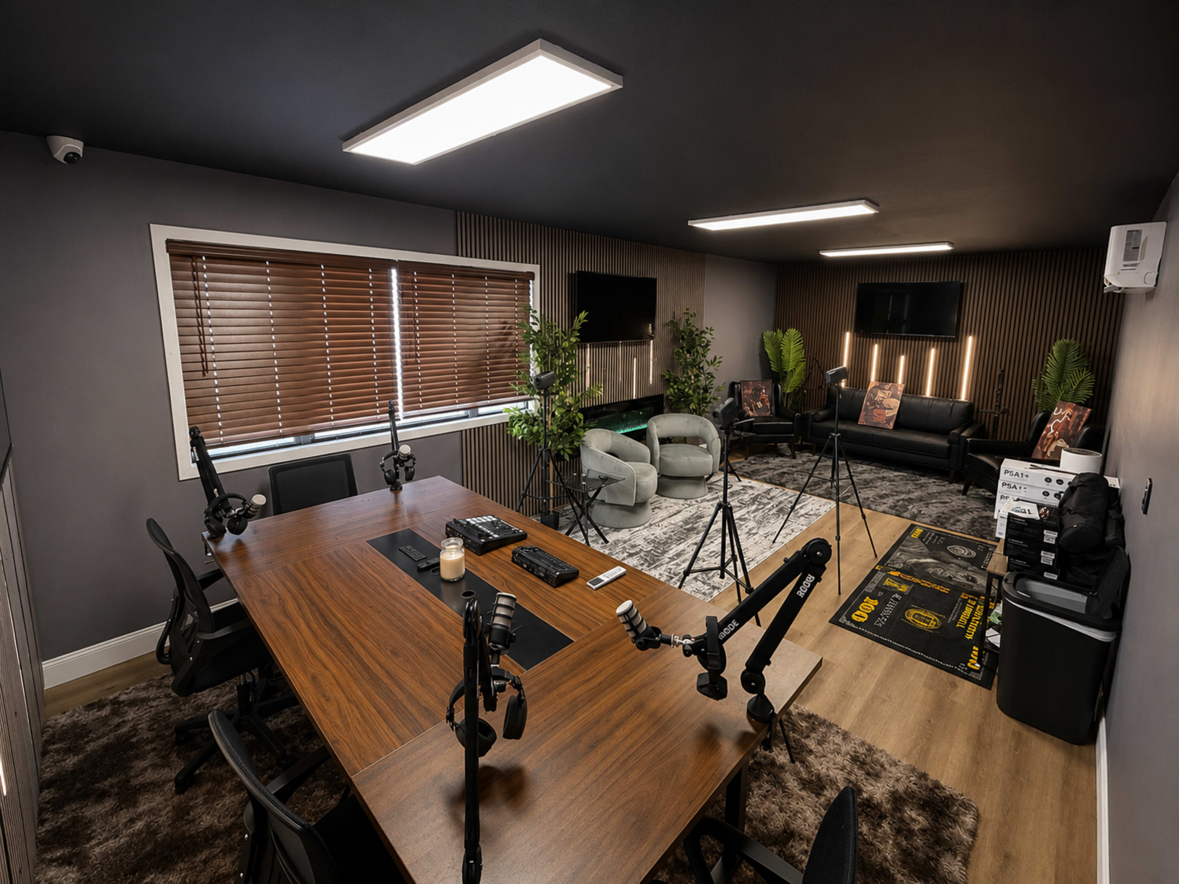 The image shows a modern office space featuring a large wooden conference table surrounded by several black chairs, with additional seating and greenery in the background.
