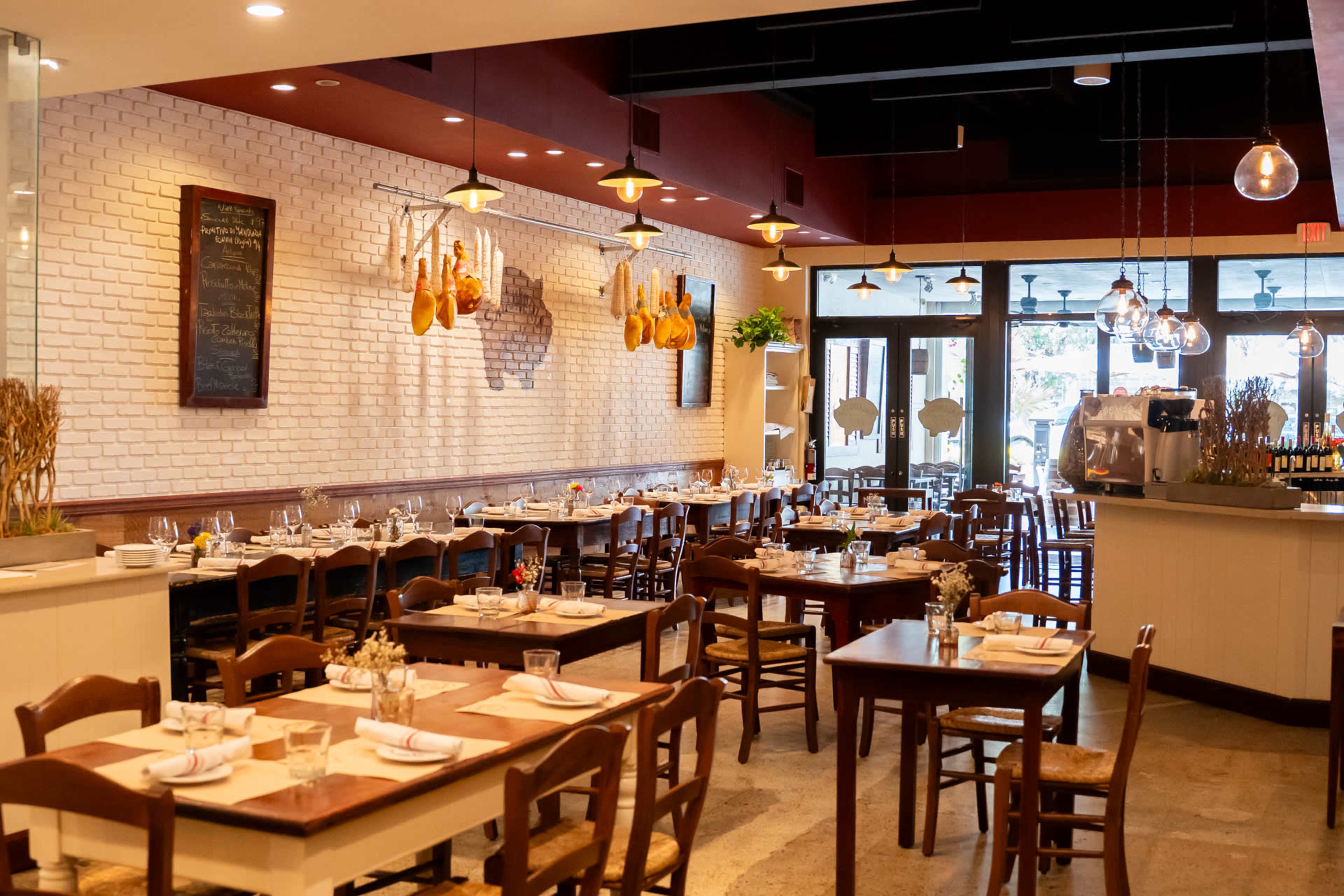 The image shows a restaurant interior with wooden tables and chairs, decorative hanging lights, and a bar area in the background.