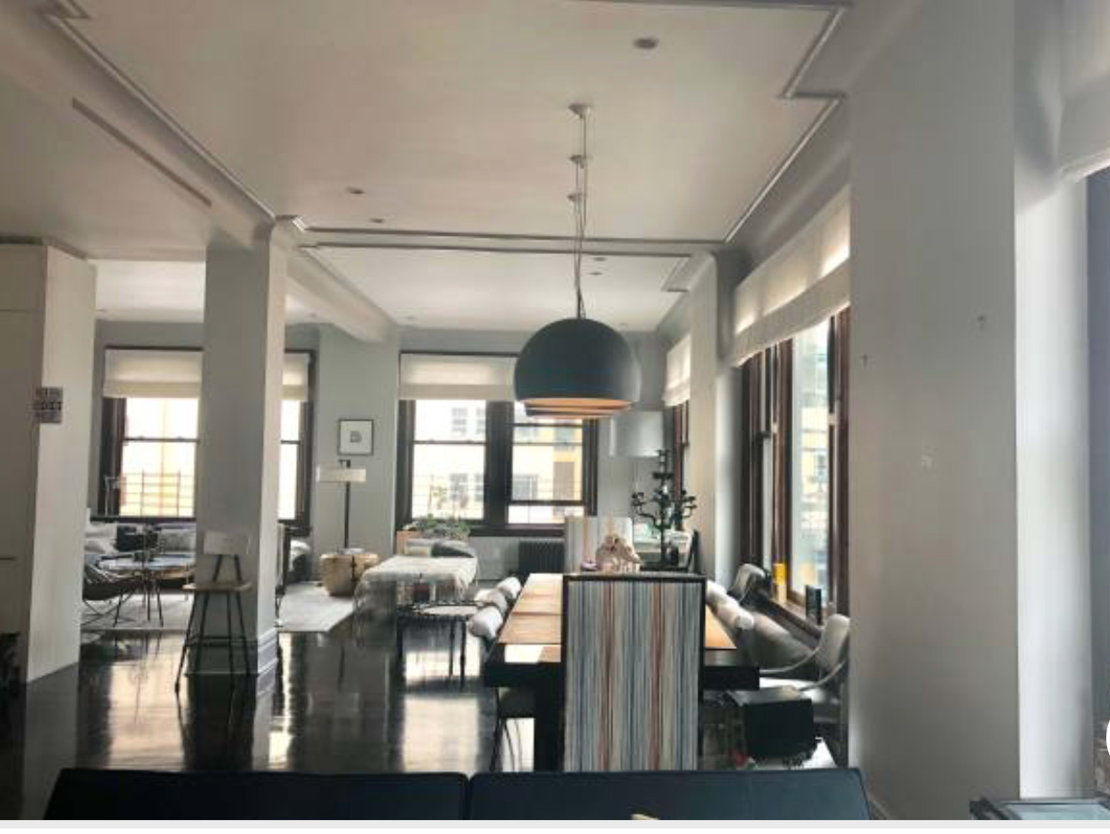 A spacious modern living area featuring large windows, a dining table with chairs, and a pendant light hanging from the ceiling.
