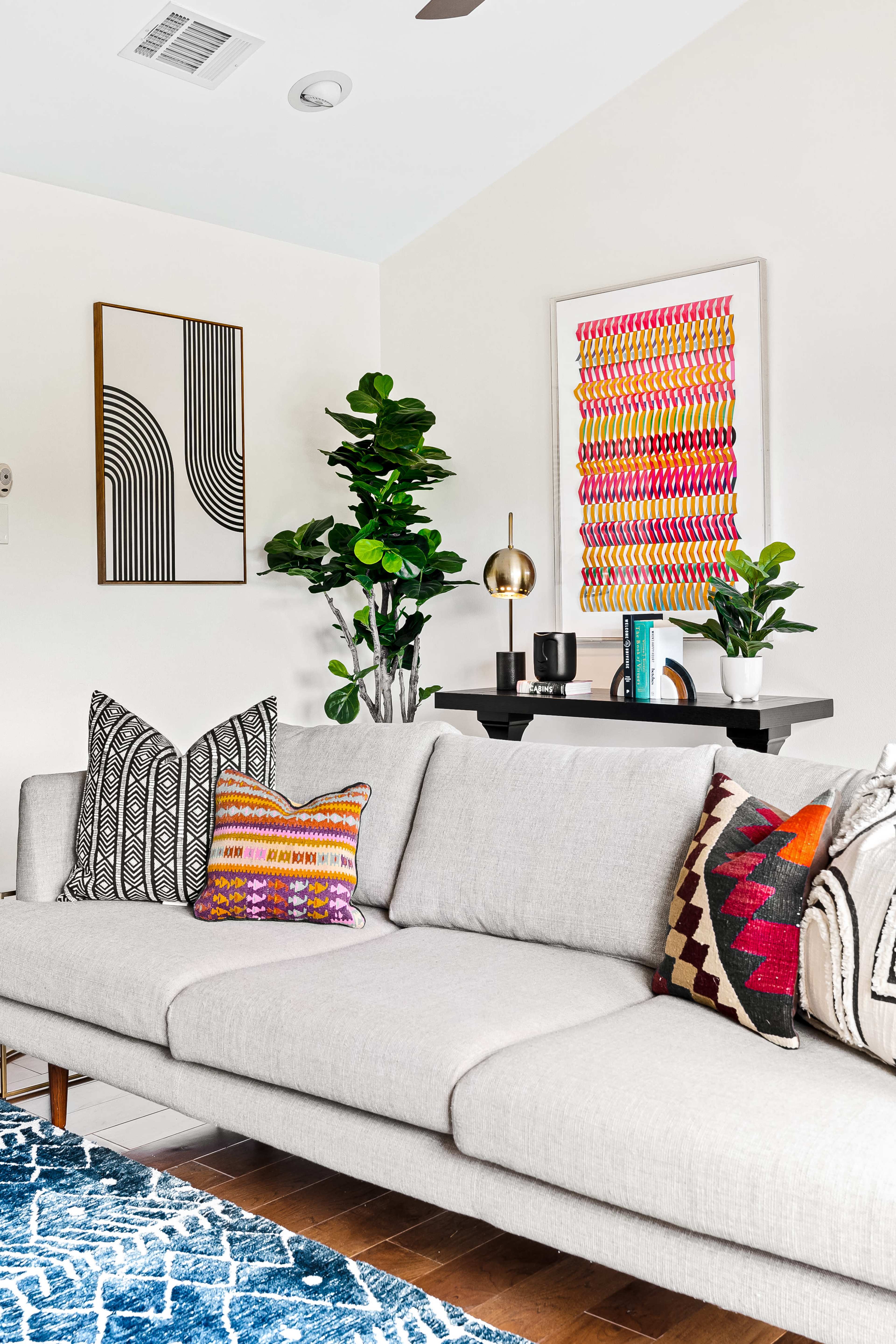 A modern living room features a light gray sofa adorned with decorative pillows, alongside a coffee table and framed artwork on the walls, complemented by indoor plants.