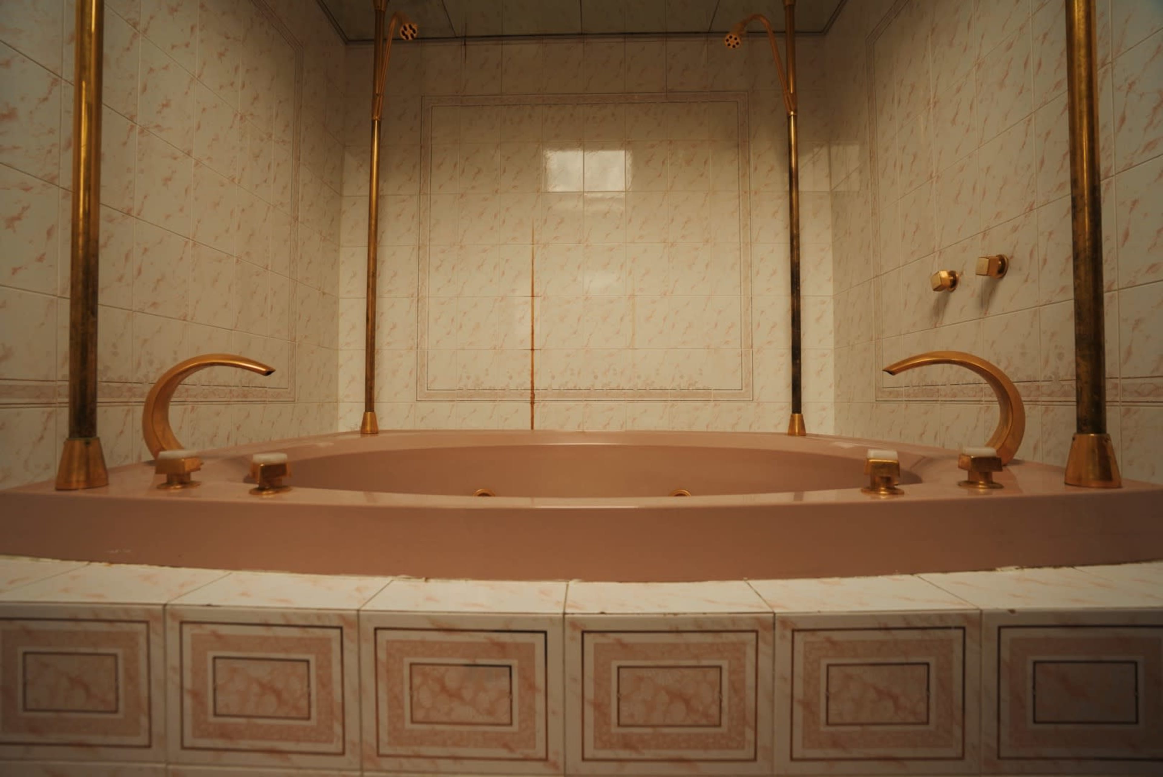 A spacious bathtub with gold fixtures set against pale marble-patterned tiles.