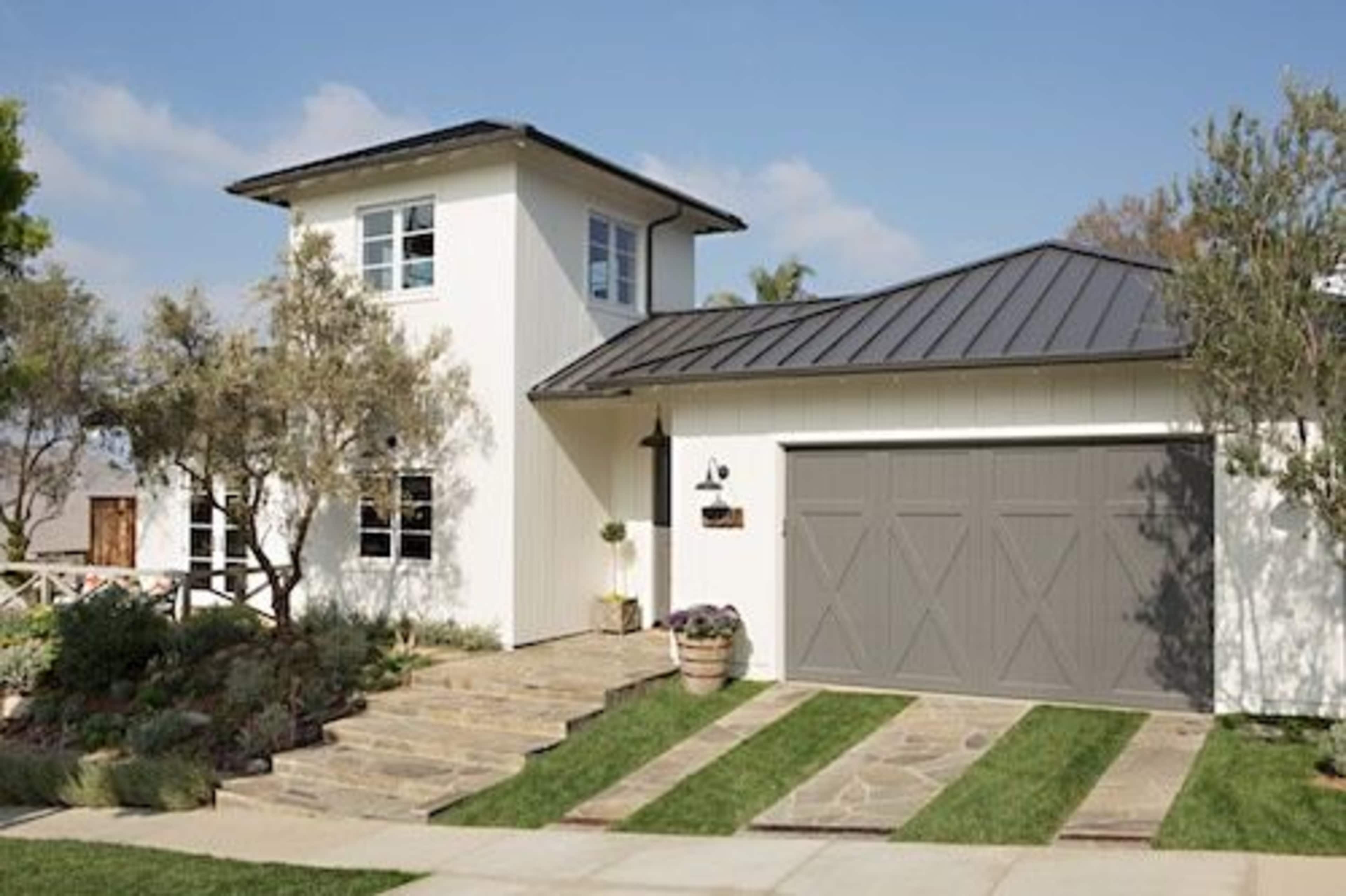 A modern house with a central tower, a metal roof, and a driveway lined with stone steps and greenery.