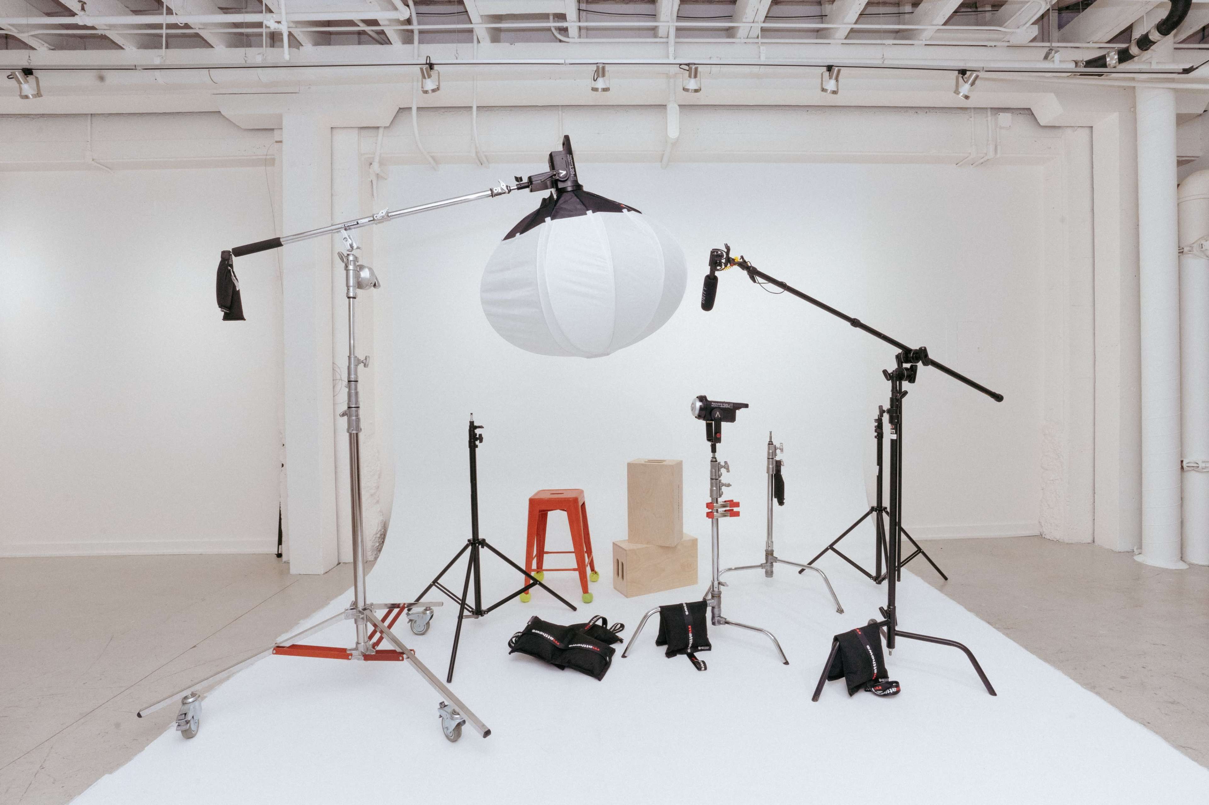 A photography studio setup features various lighting equipment, microphones, and props arranged on a white backdrop.
