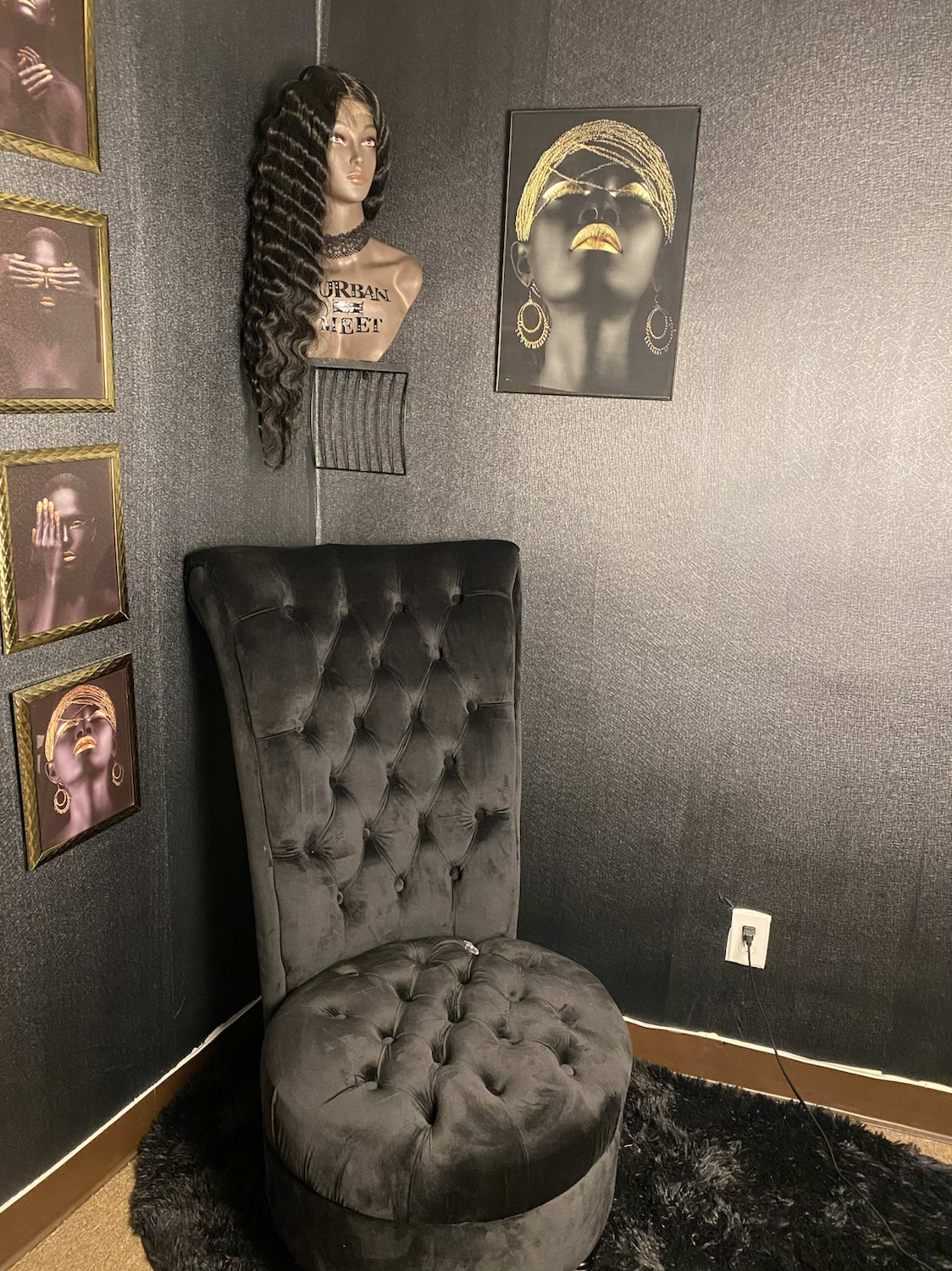 A velvet black chair next to a wall adorned with framed portraits and a mannequin head displaying long, curly hair.