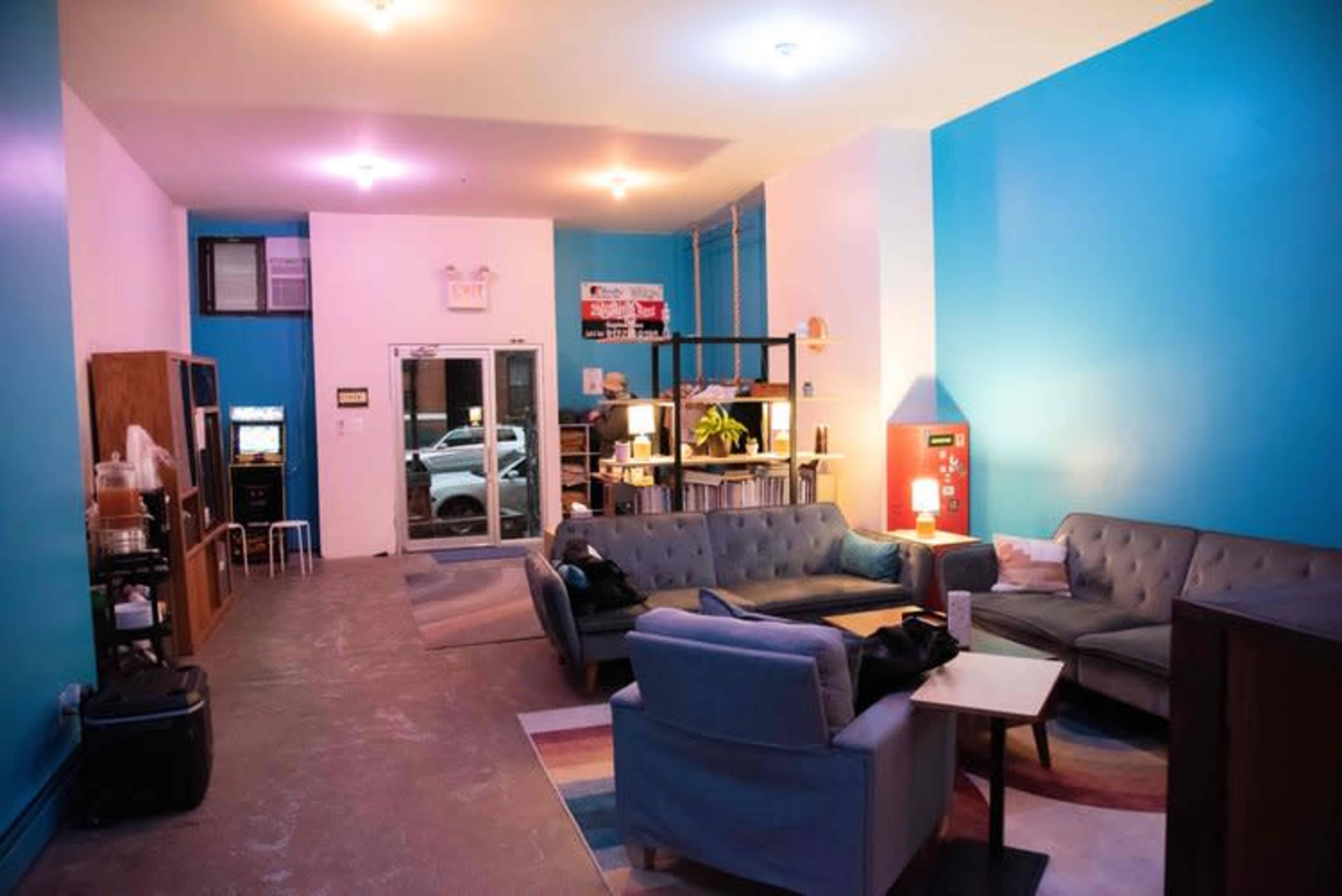 A spacious lounge area with blue walls, various seating arrangements, and a large window facing the street.