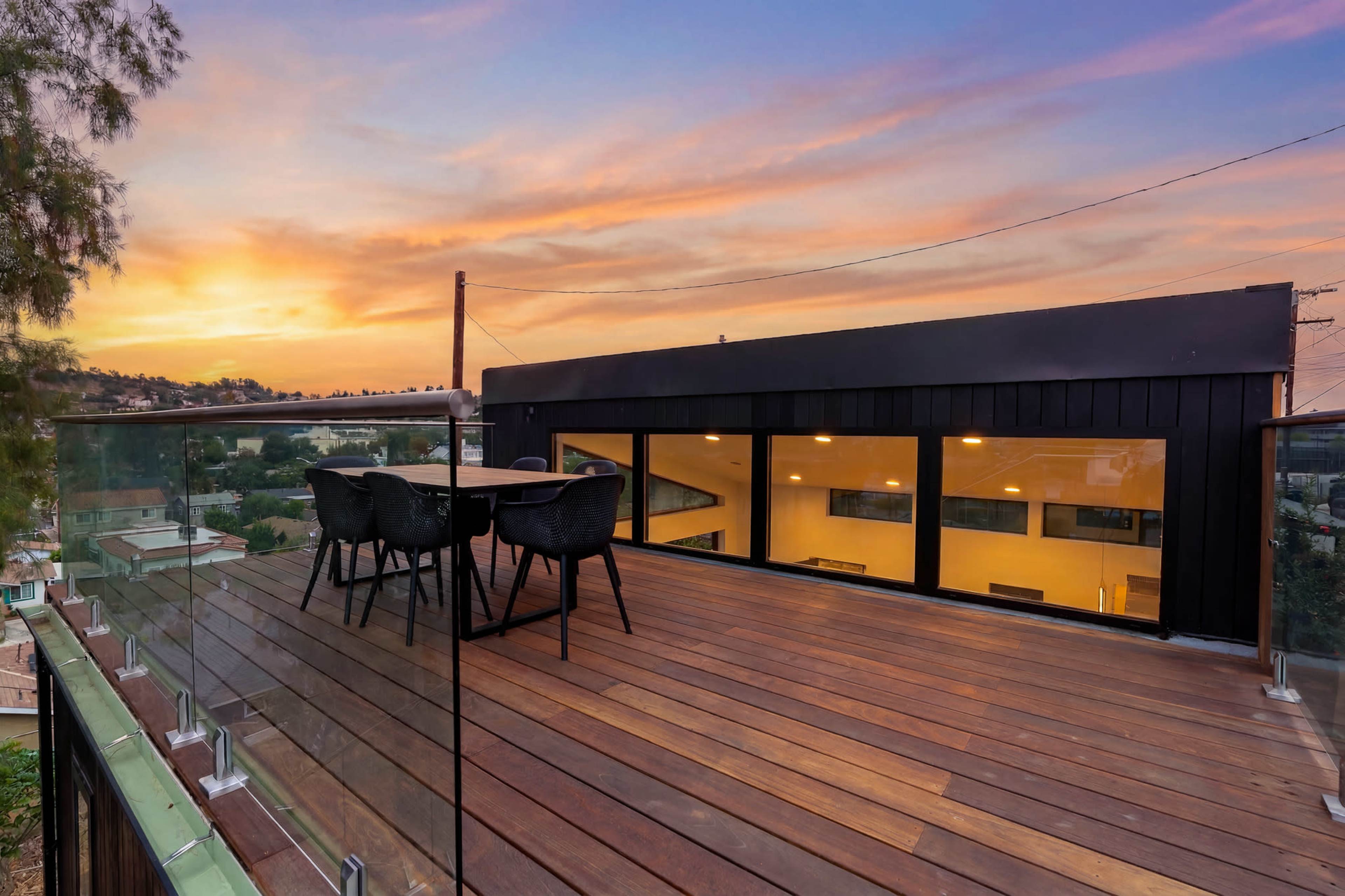 A modern rooftop deck features a dining table and chairs, overlooking a sunset view.