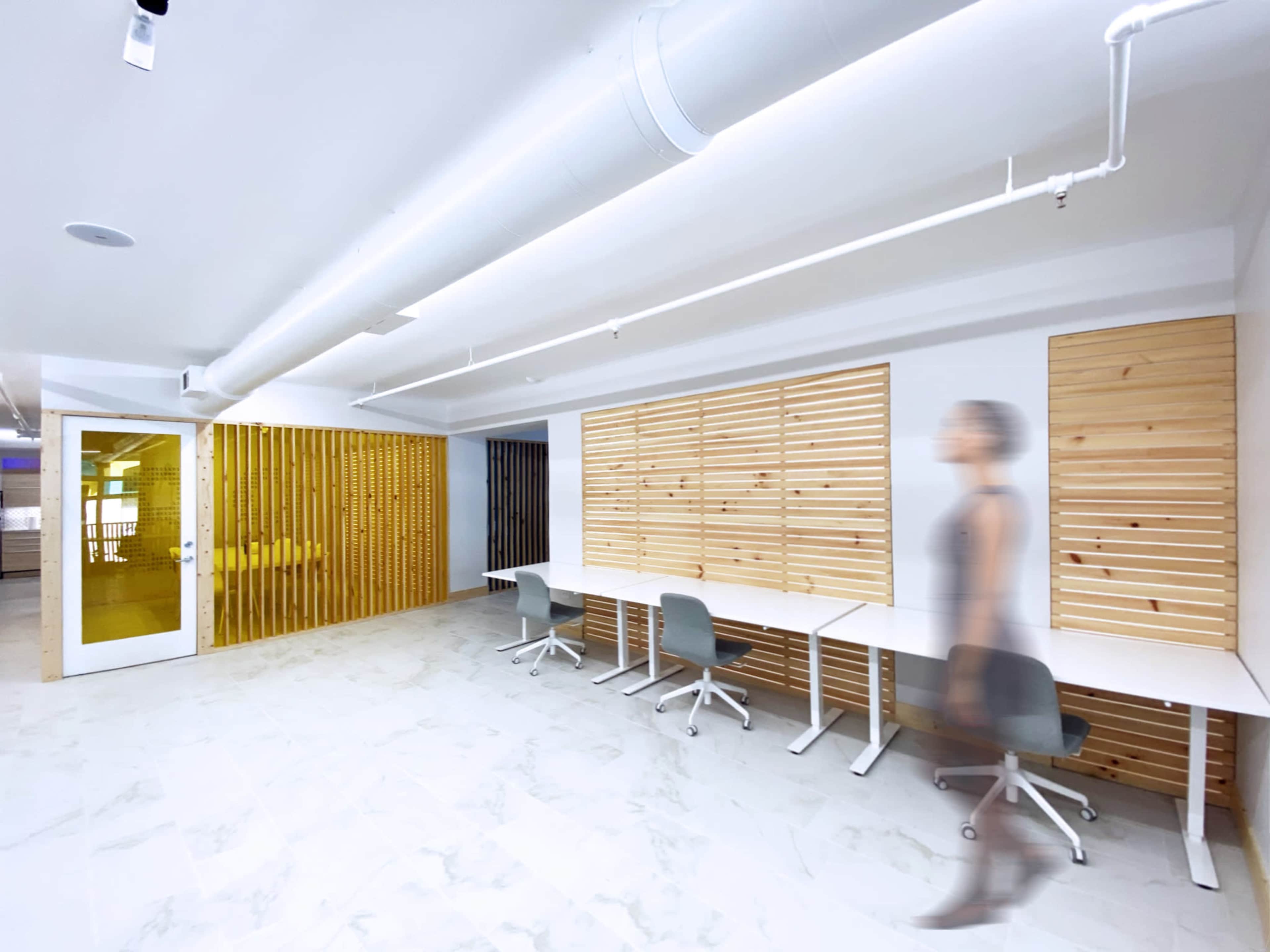 A modern office space features wooden paneling, white desks, and a person in motion.