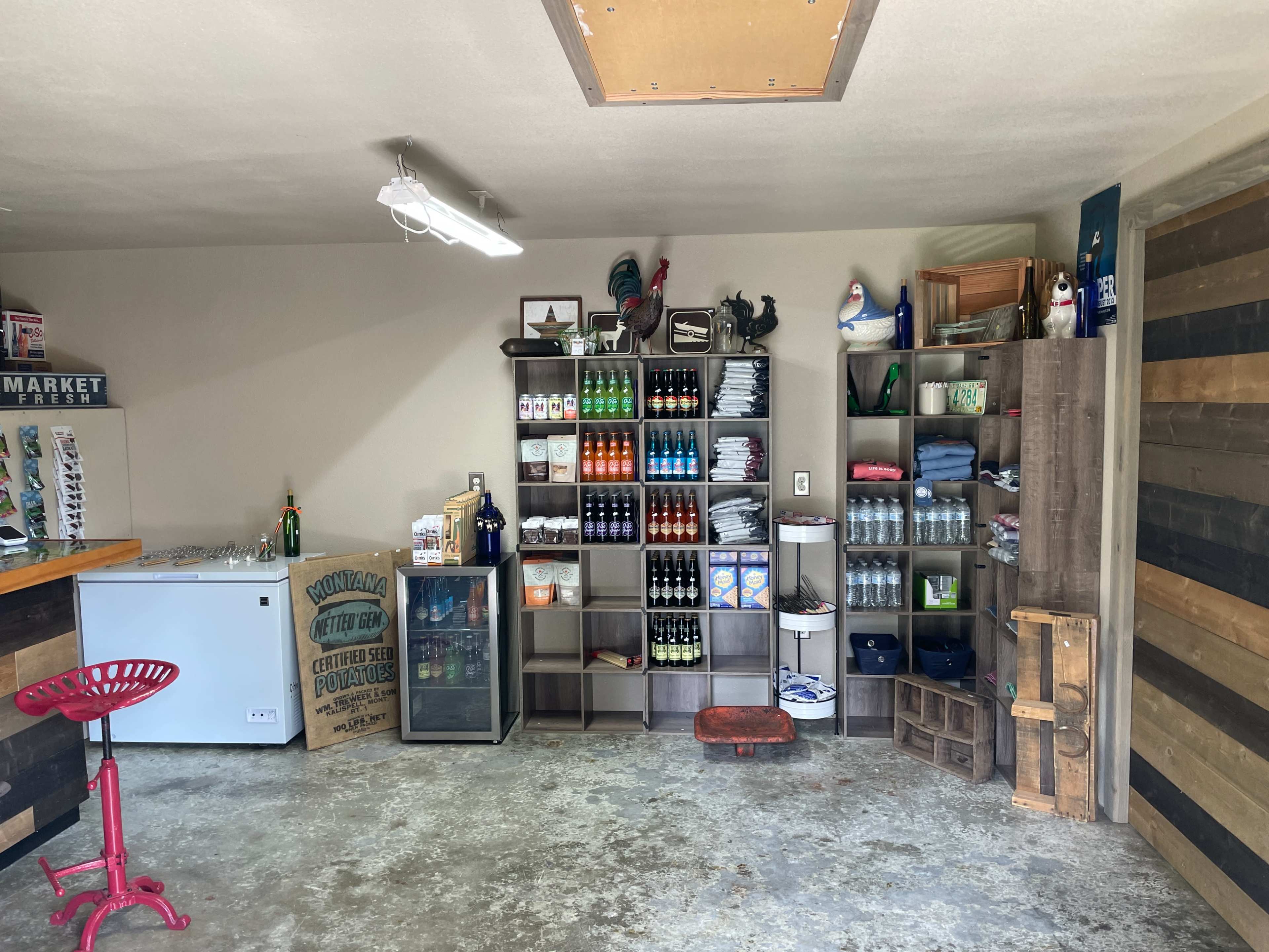 A garage interior with shelving units filled with various products, a small bar area, and a cooler.