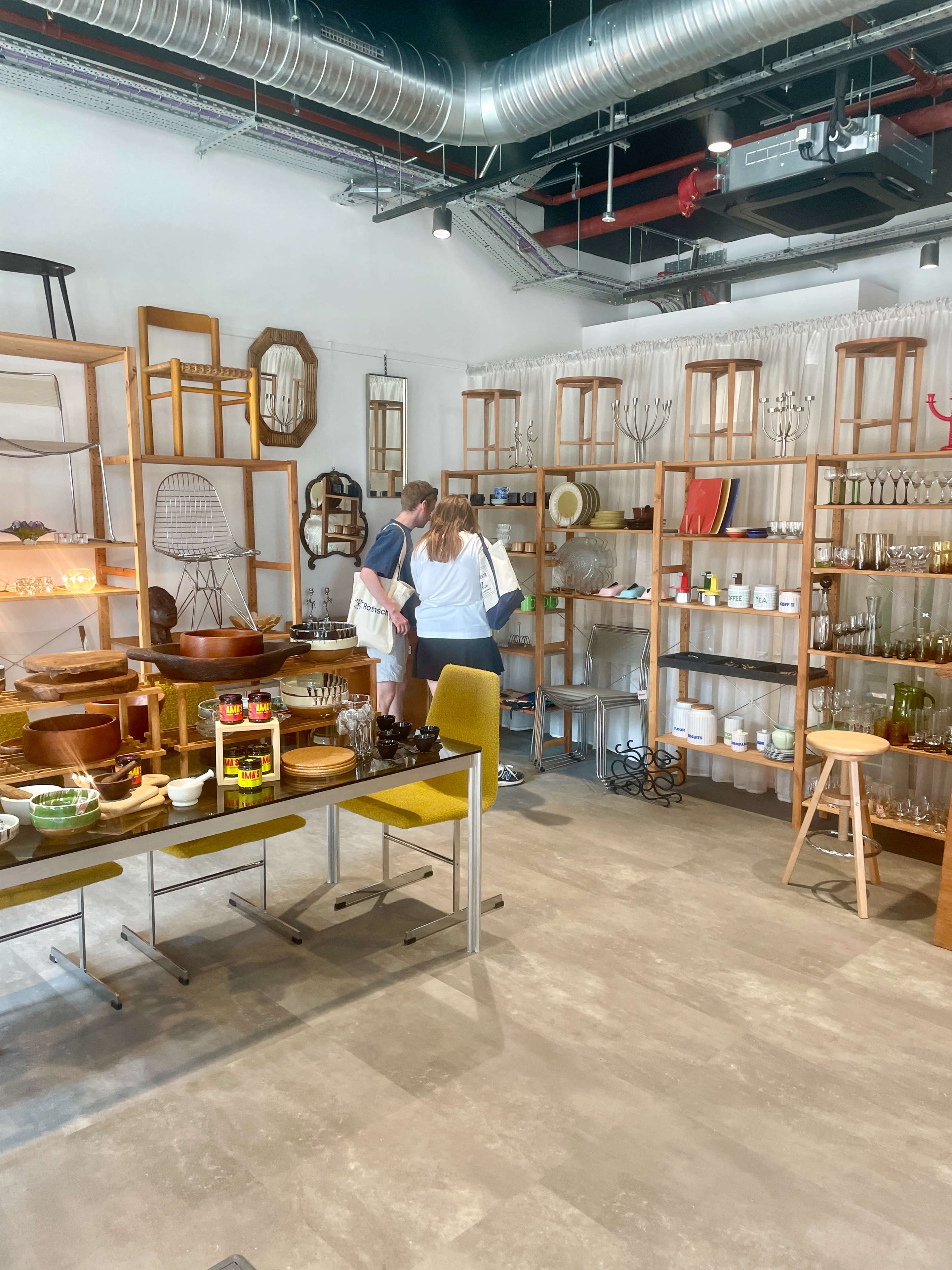 A couple is exploring a modern store filled with various kitchenware and home decor items displayed on wooden shelves.