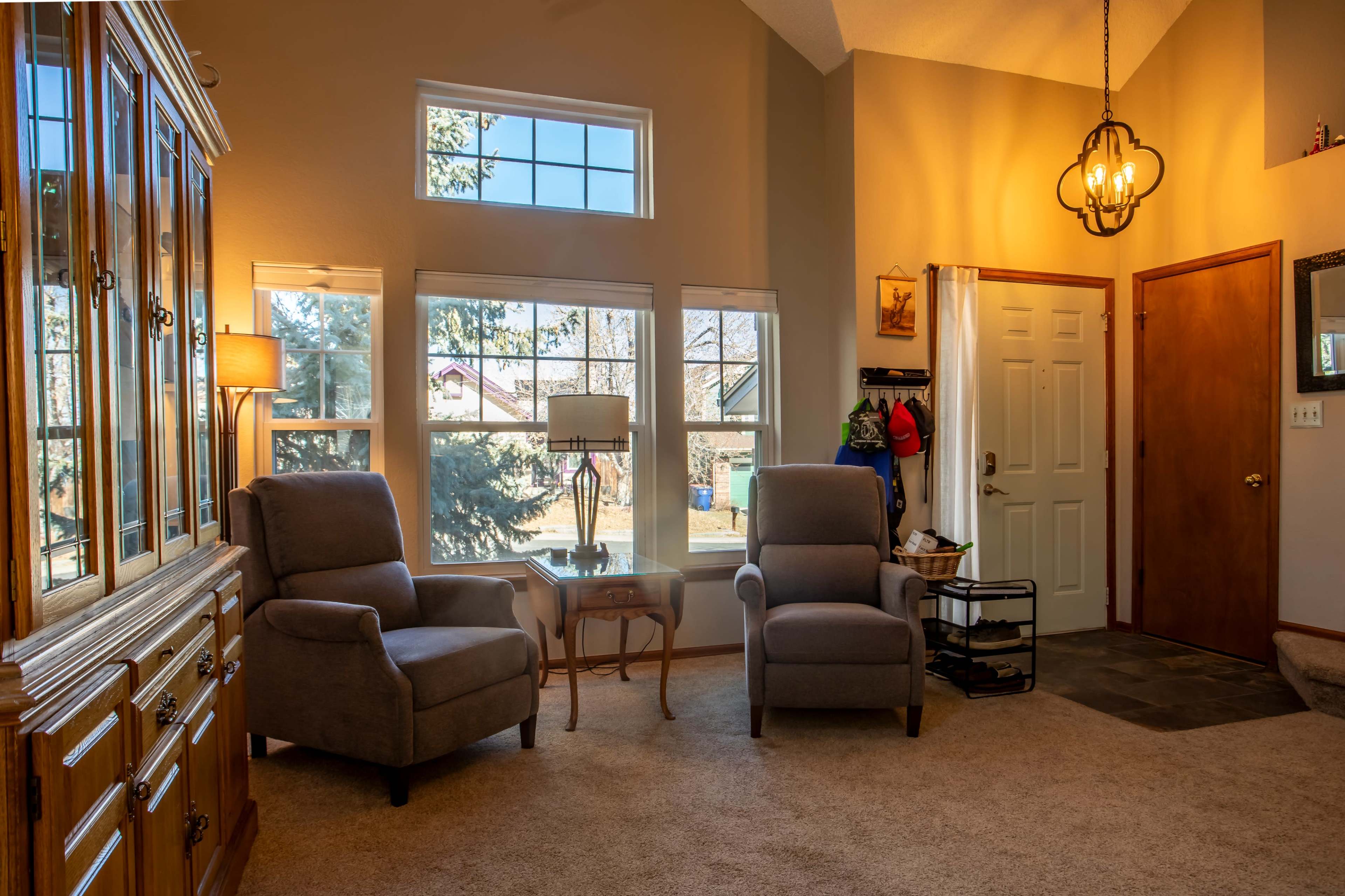 The living room features two gray armchairs, a wooden cabinet, and a front door with large windows allowing natural light.