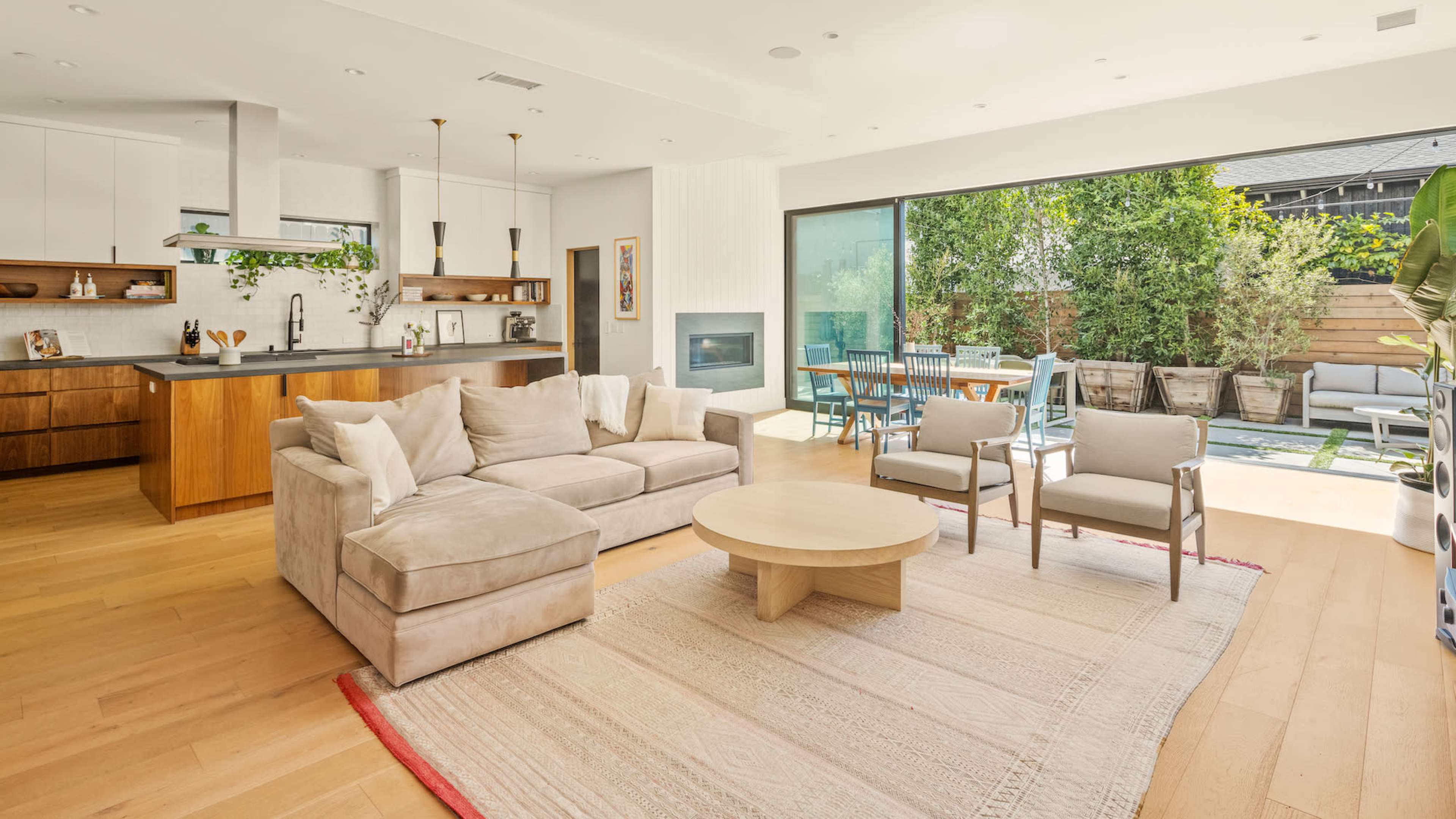 A modern living room features a light-colored sectional sofa, a round coffee table, and large sliding glass doors leading to an outdoor patio area.