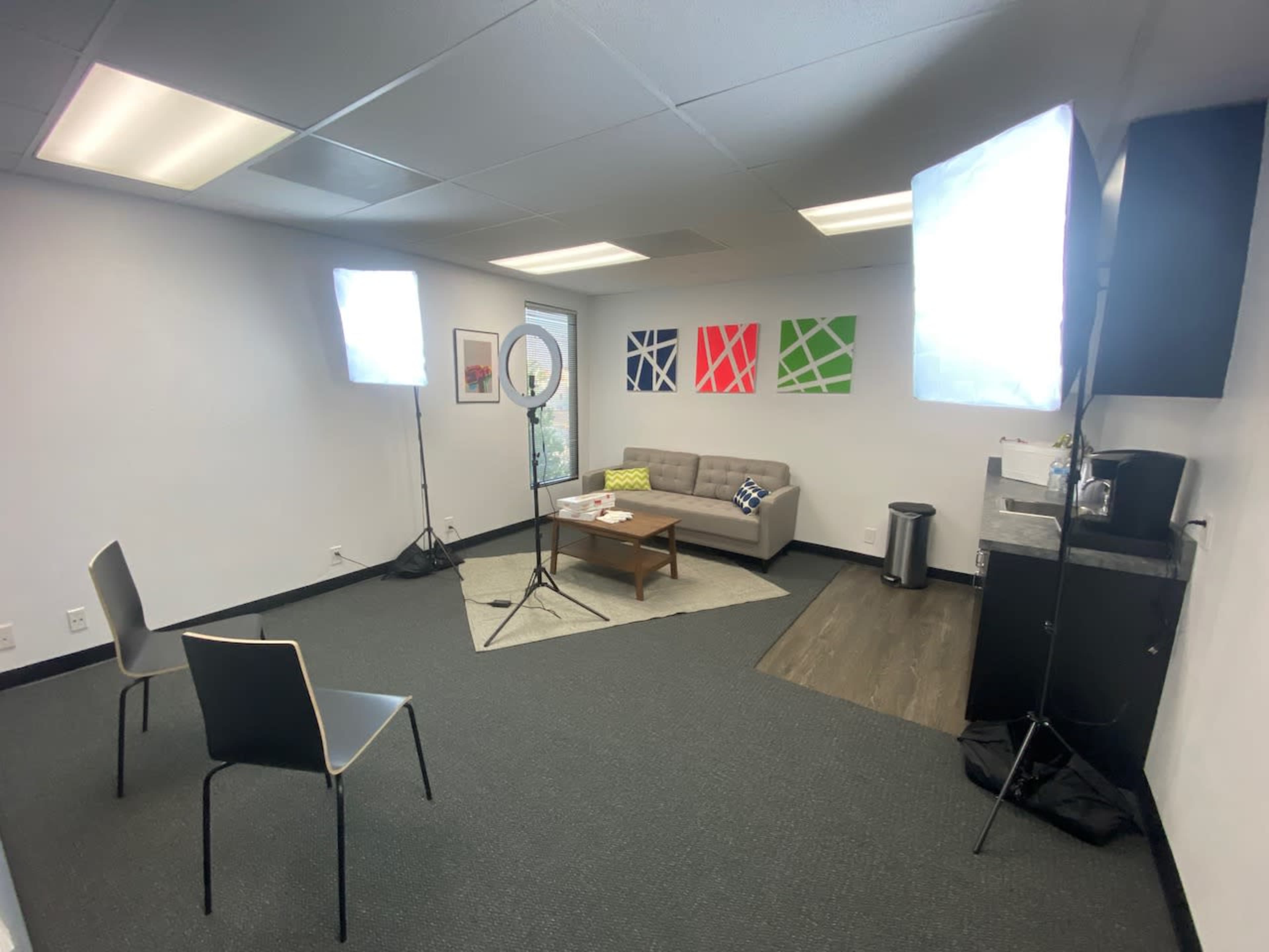 A well-lit office space with a gray couch, two chairs, and studio lighting setup around a small coffee table.