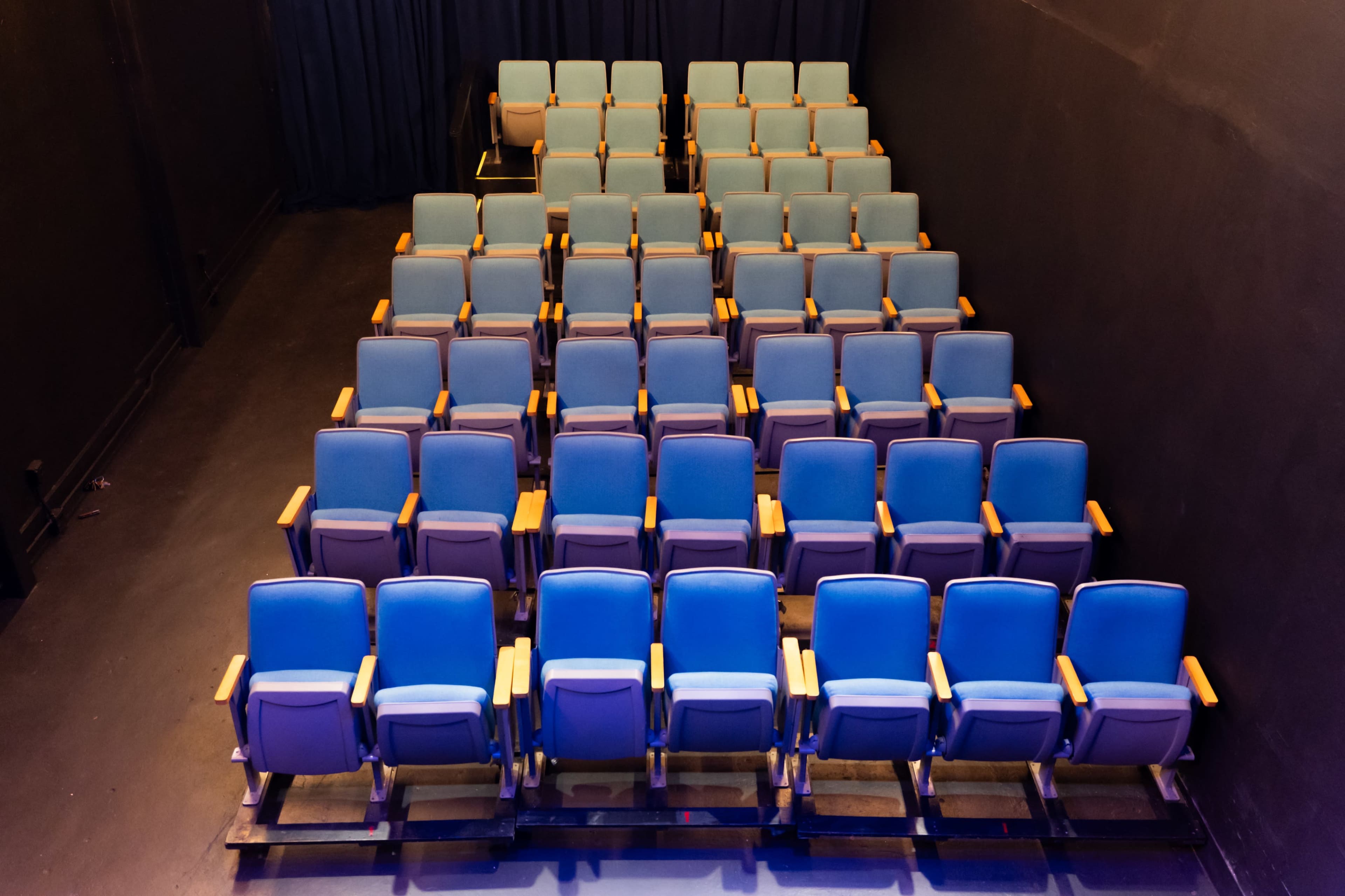 The image shows a row of empty blue theater seats arranged in a semi-stacked formation against a dark background.