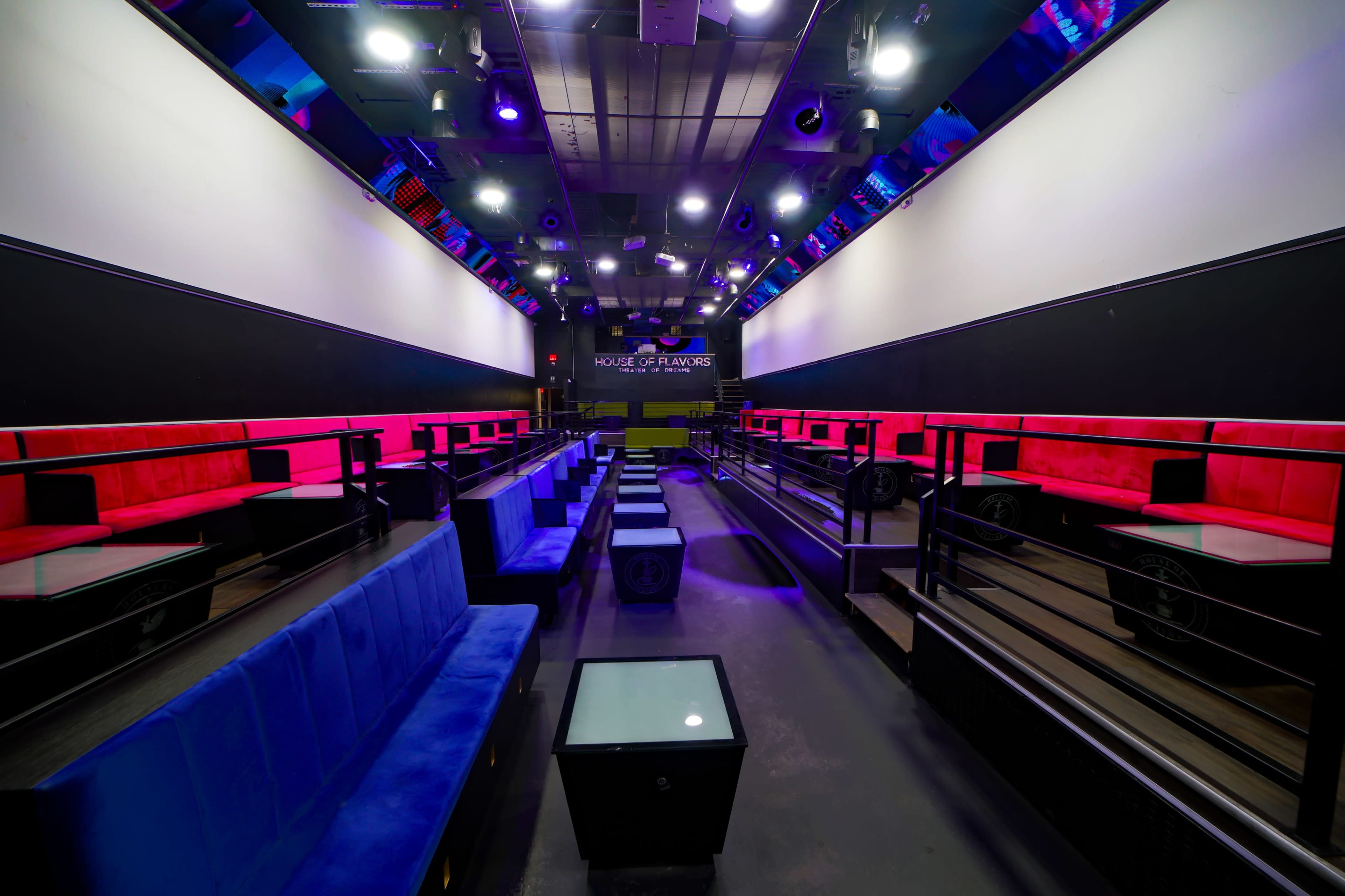 The image shows a modern venue with rows of colorful seating and ambient lighting, designed for entertainment.