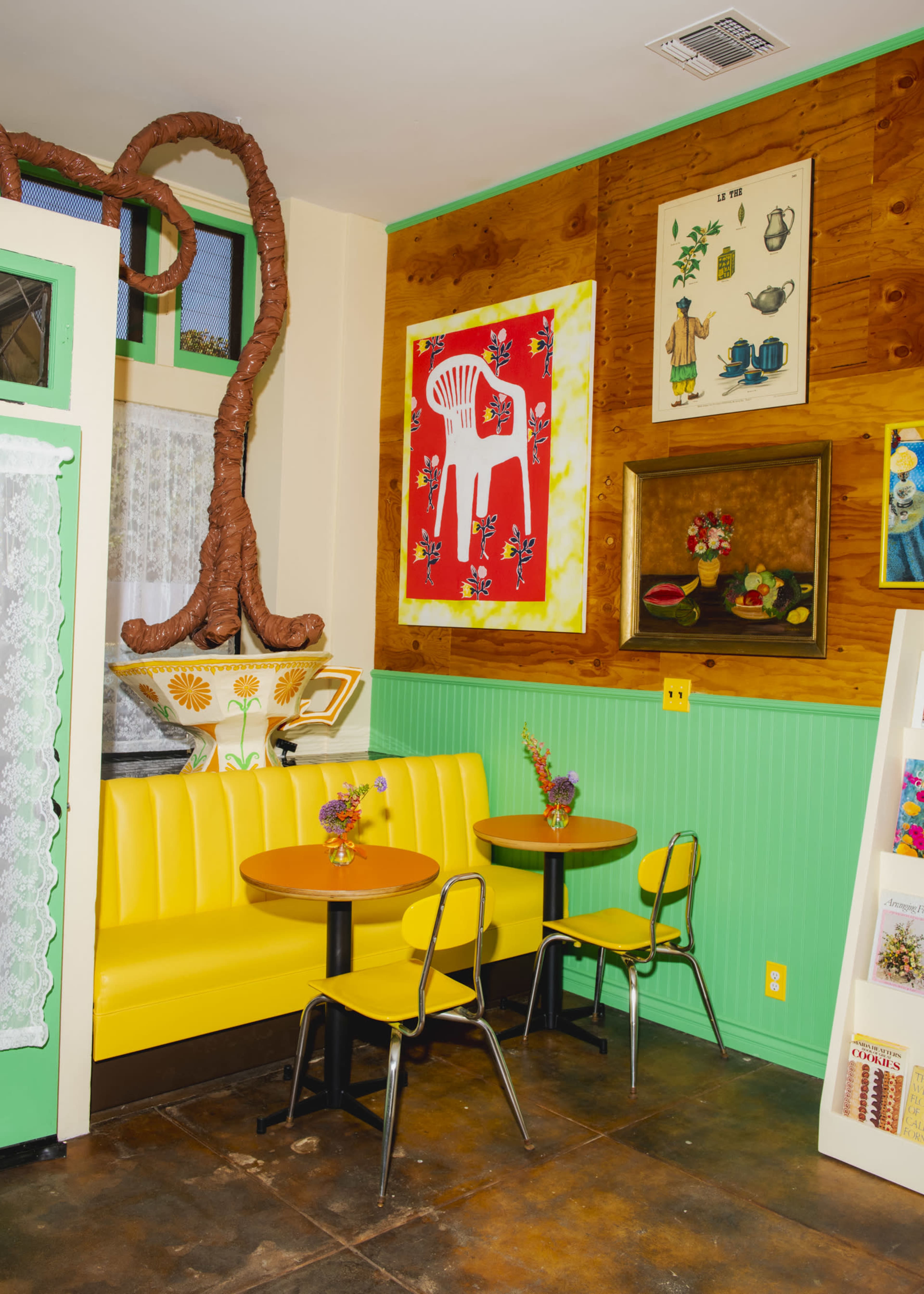 The image shows a brightly decorated café interior with yellow tables and chairs, green walls, and eclectic artwork adorning the space.
