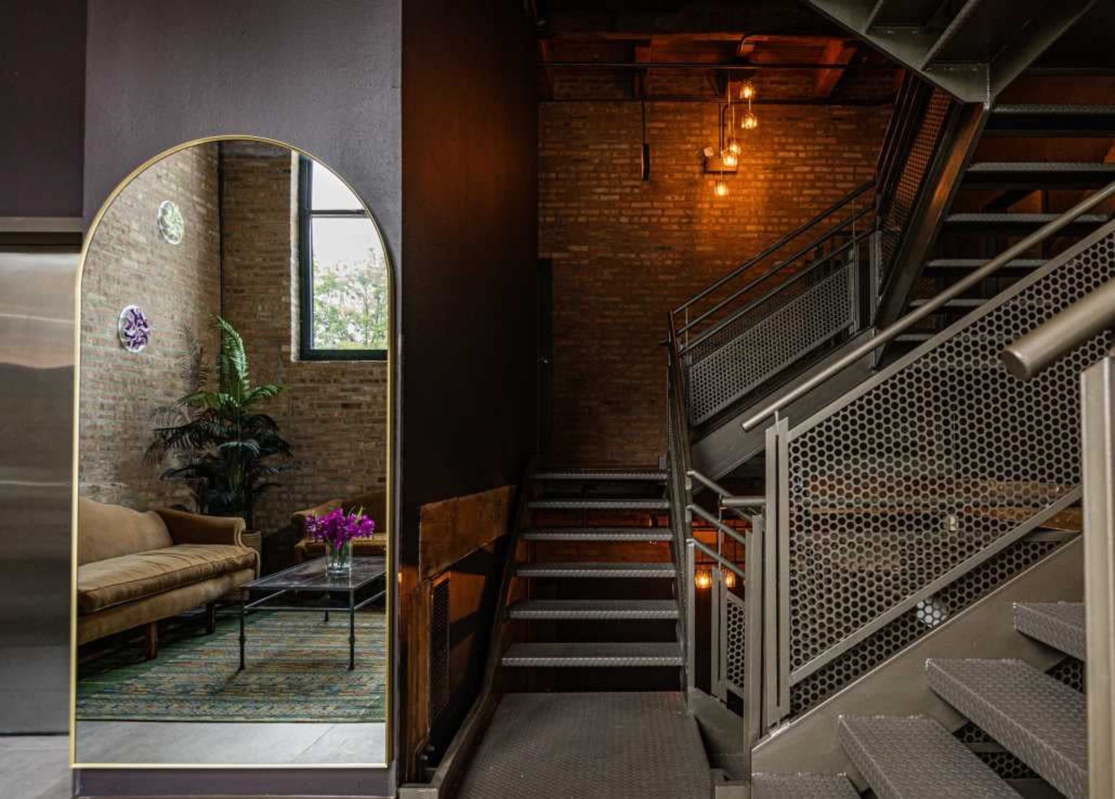 A staircase with metal railings leads to an upper level, while a mirror with a curved frame reflects a seating area with a couch and a coffee table.
