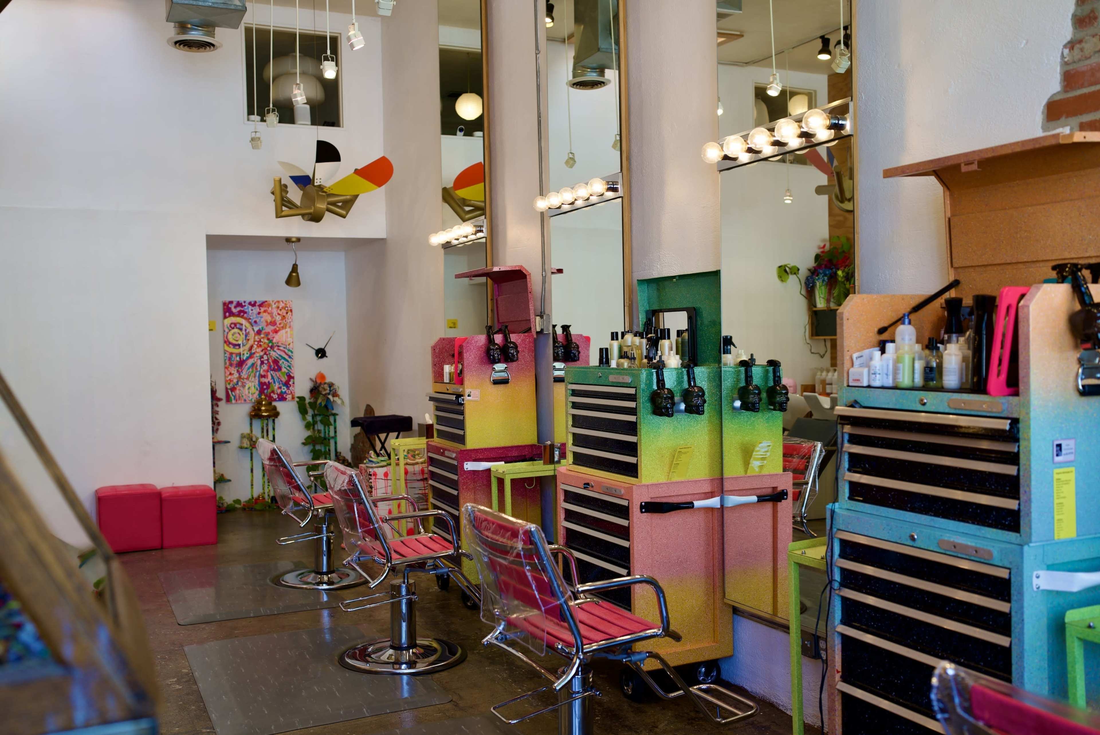 The image shows a brightly colored hair salon featuring multiple styling stations with chairs and storage units against a backdrop of modern decor.