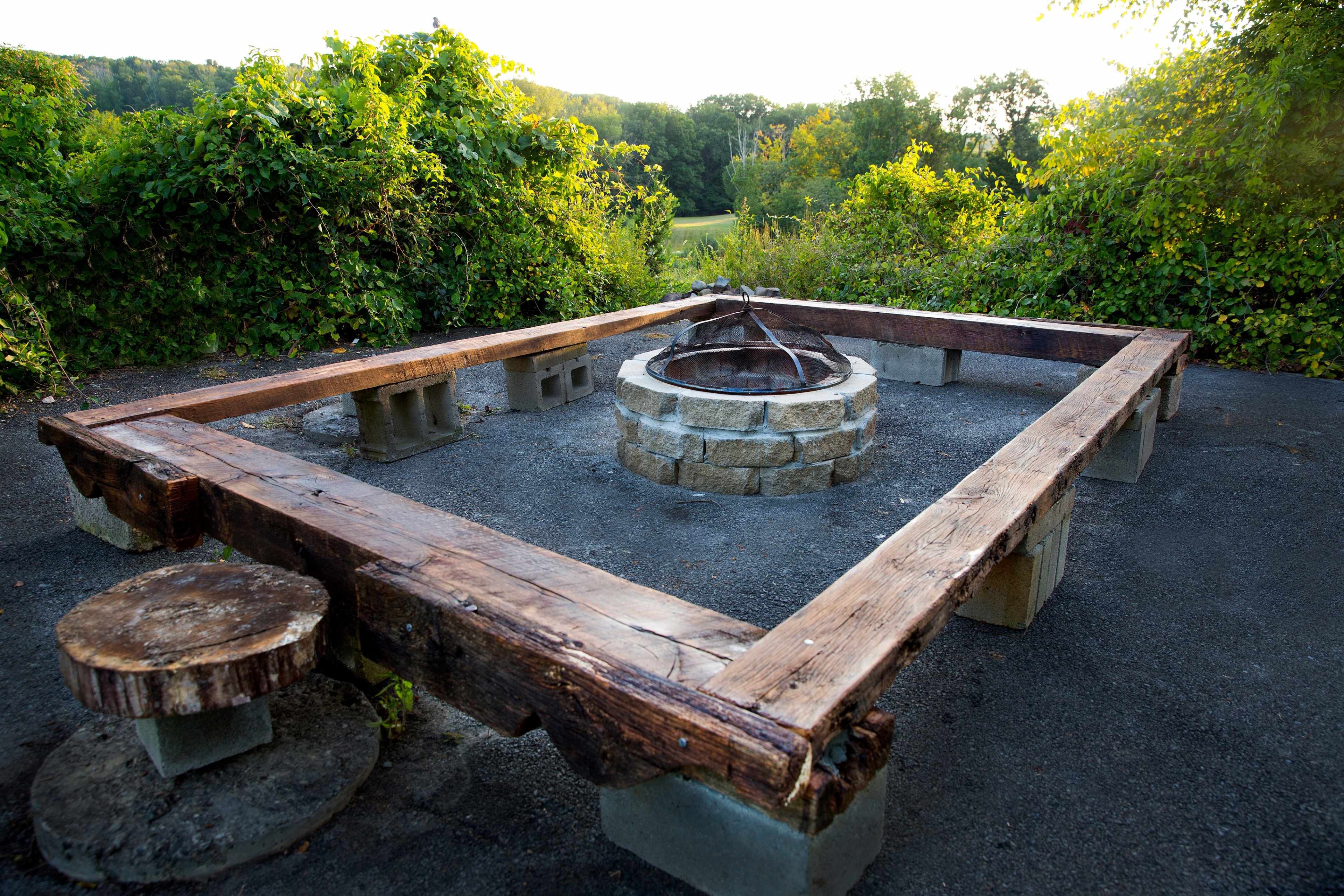 A rectangular fire pit surrounded by wooden seating and stone blocks, set in a natural landscape.