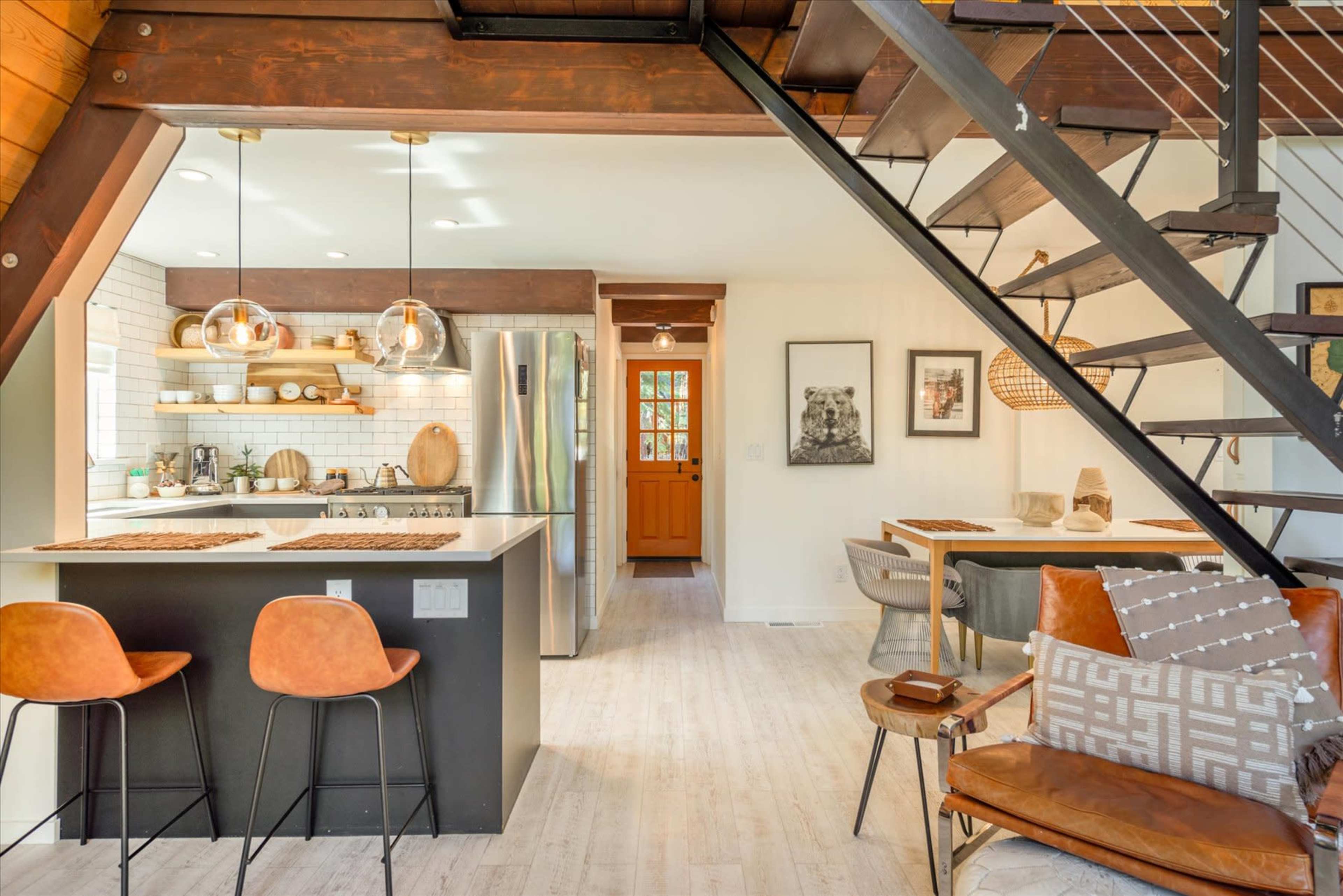 The image shows a modern interior of a home featuring a kitchen with a dining area, a staircase, and various furnishings.
