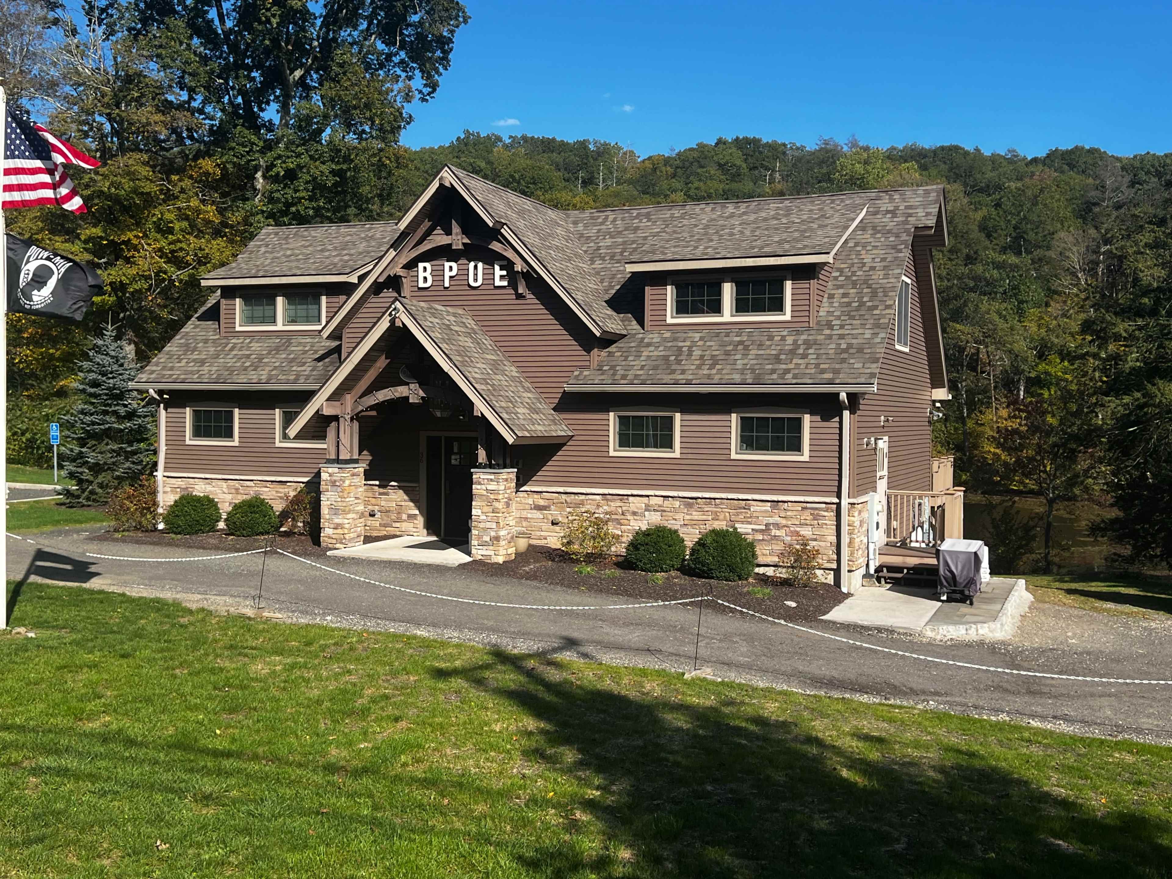 A large brown wooden lodge-style building with a stone foundation, surrounded by a green lawn and trees in the background.