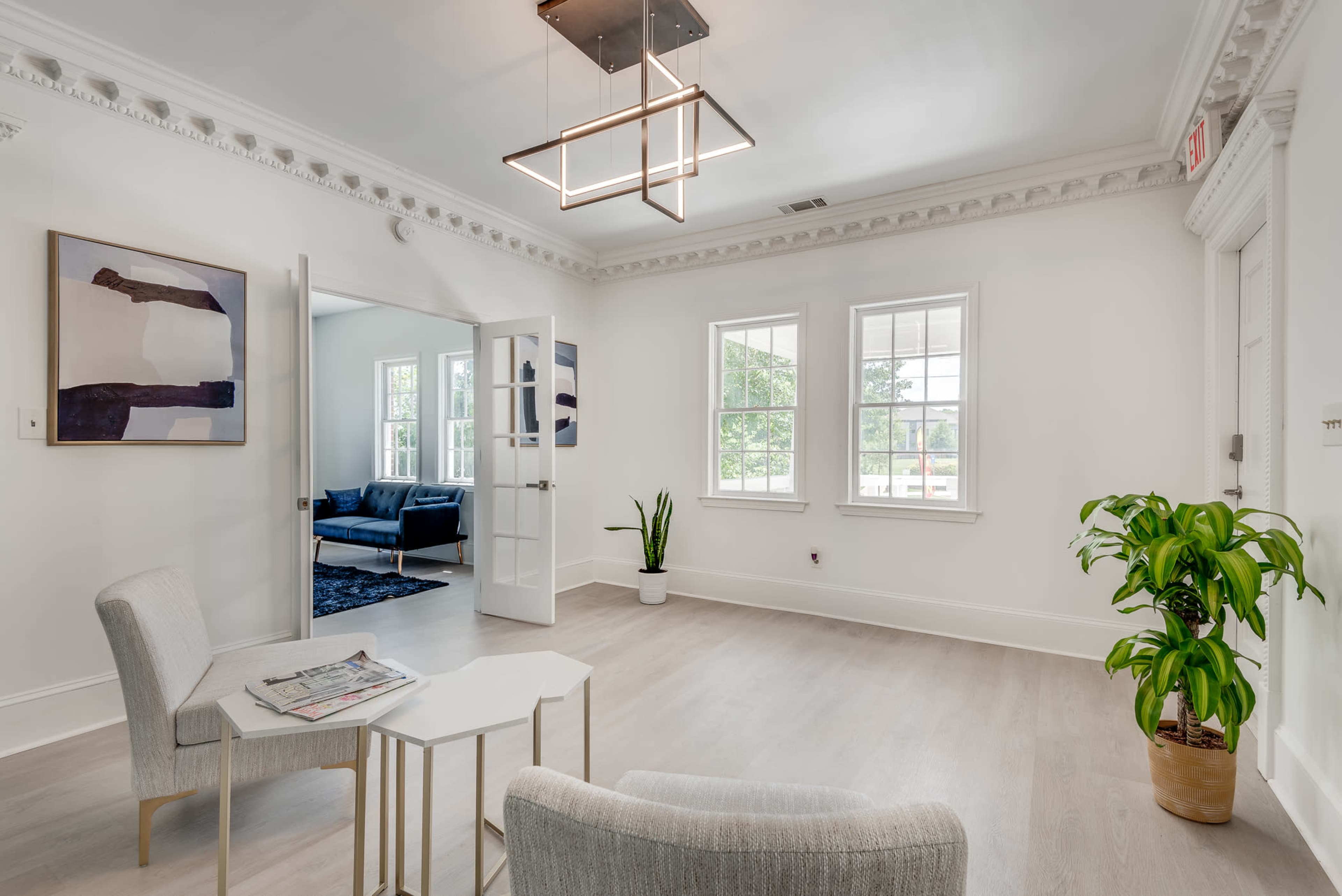 A bright, modern interior space with two chairs and a small table, featuring large windows and a doorway leading to another room.