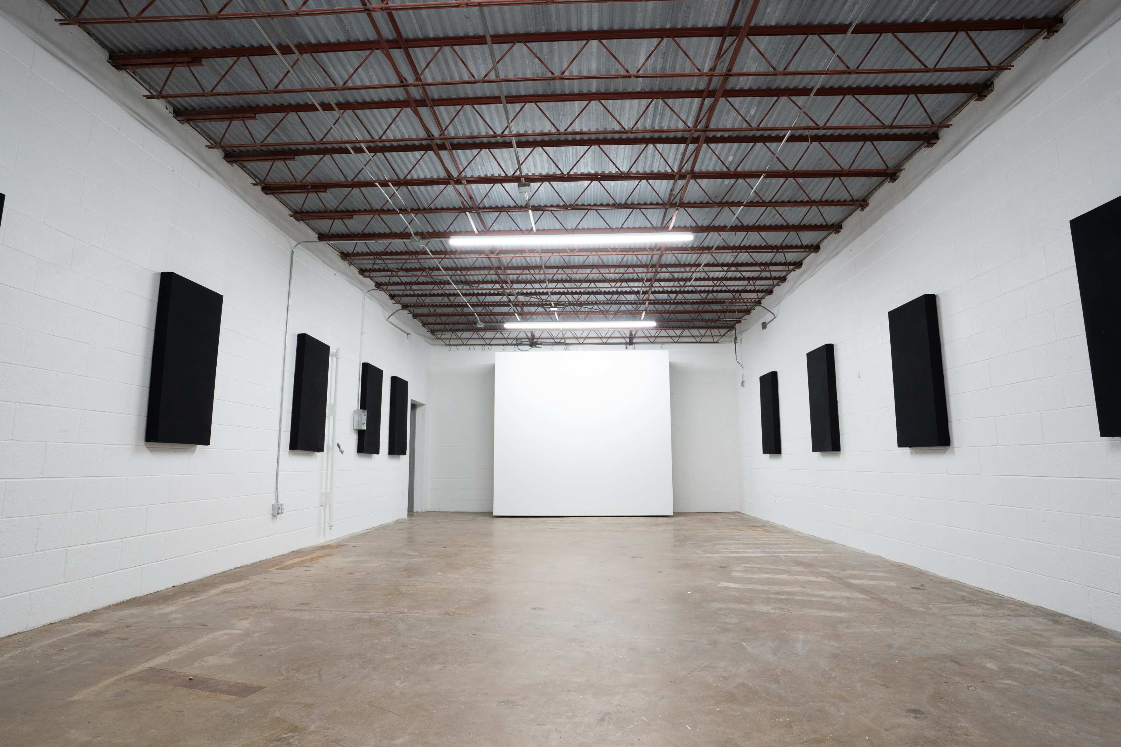 The image shows a minimalist art gallery featuring white walls and a large white display area surrounded by black rectangular canvases hung on the walls.